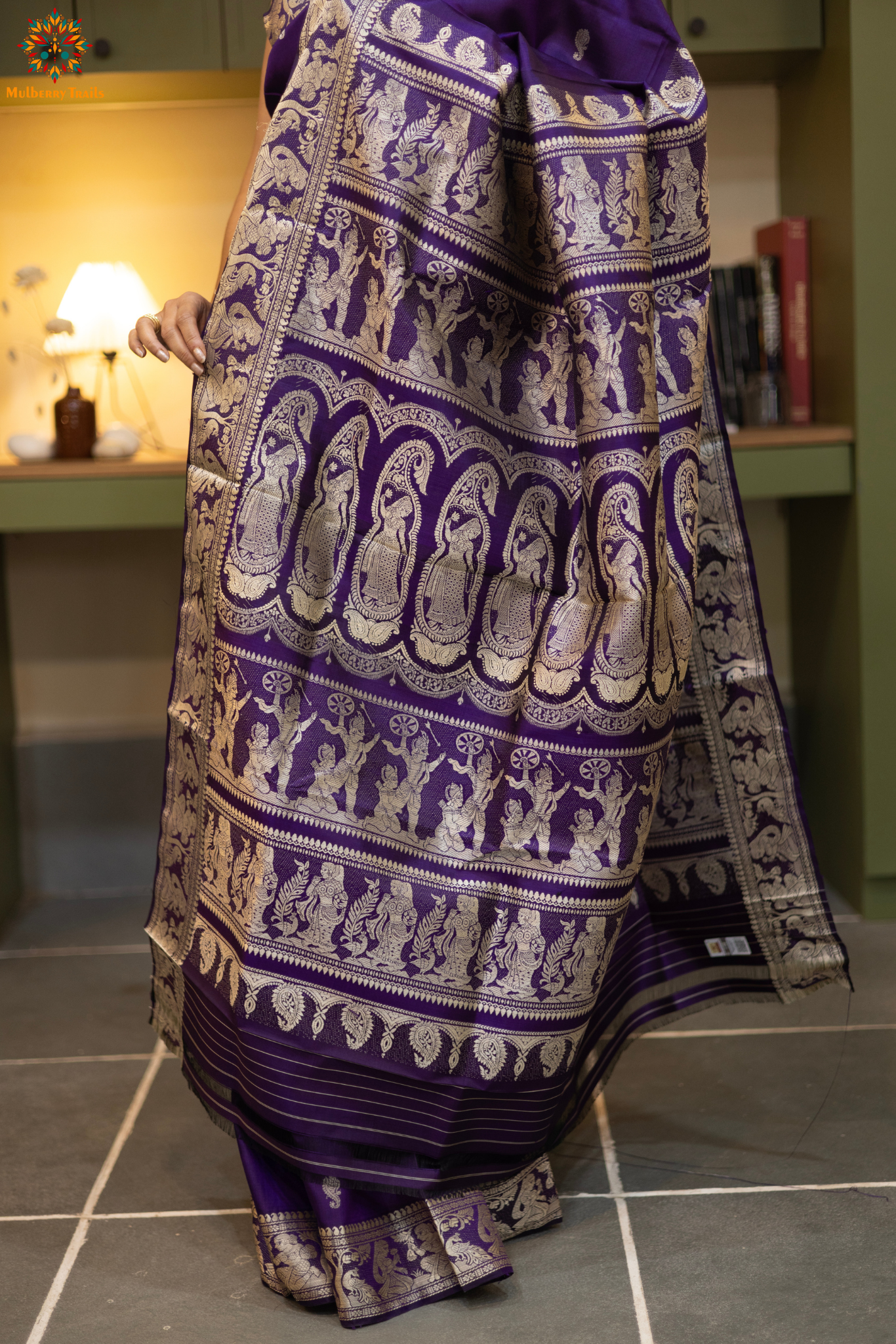 Woman wearing a traditional baluchari saree in a room with a desk and lamp. Woman in a carrot red and silver resham work saree standing indoors with a desk and lamp in the background.
Baluchari – Pure Silk Baluchari Saree
1. “Pure silk Baluchari saree with temple motif weave and Silver resham detailing for a regal look.”
2. “Silk Mark pure silk saree featuring intricate gold resham work motifs and rich texture.