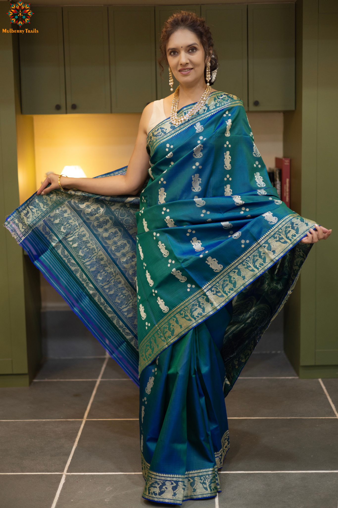 Woman wearing a traditional baluchari saree in a room with a desk and lamp. Woman in a Peacock blue and silver resham work saree standing indoors with a desk and lamp in the background.
Baluchari – Pure Silk Baluchari Saree
1. “Pure silk Baluchari saree with meenakari motif weave and Silver resham detailing for a regal look.”
2. “Silk Mark pure silk meenakari saree featuring intricate gold resham work motifs and rich texture.