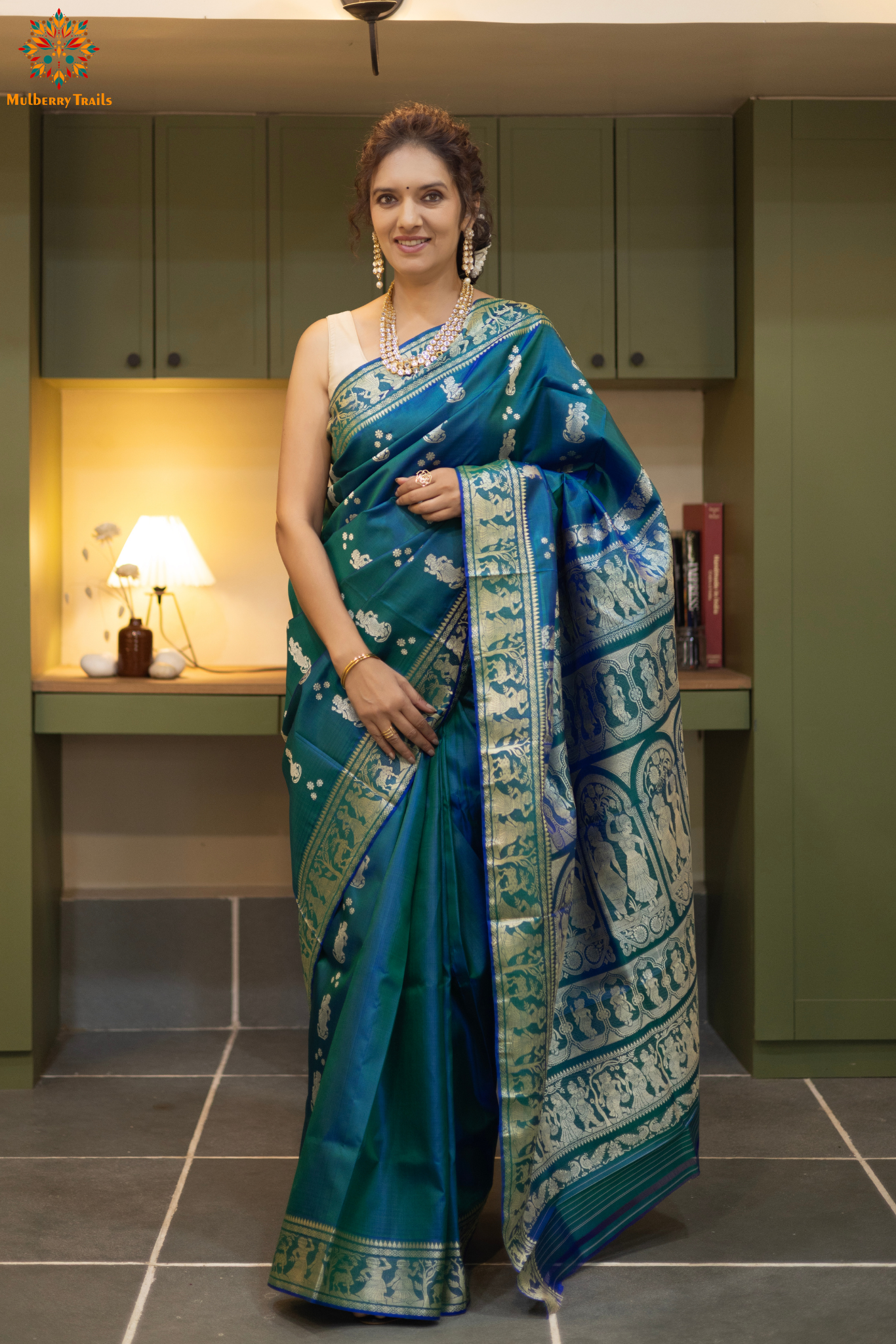 Woman wearing a traditional baluchari saree in a room with a desk and lamp. Woman in a Peacock blue and silver resham work saree standing indoors with a desk and lamp in the background.
Baluchari – Pure Silk Baluchari Saree
1. “Pure silk Baluchari saree with meenakari motif weave and Silver resham detailing for a regal look.”
2. “Silk Mark pure silk meenakari saree featuring intricate gold resham work motifs and rich texture.