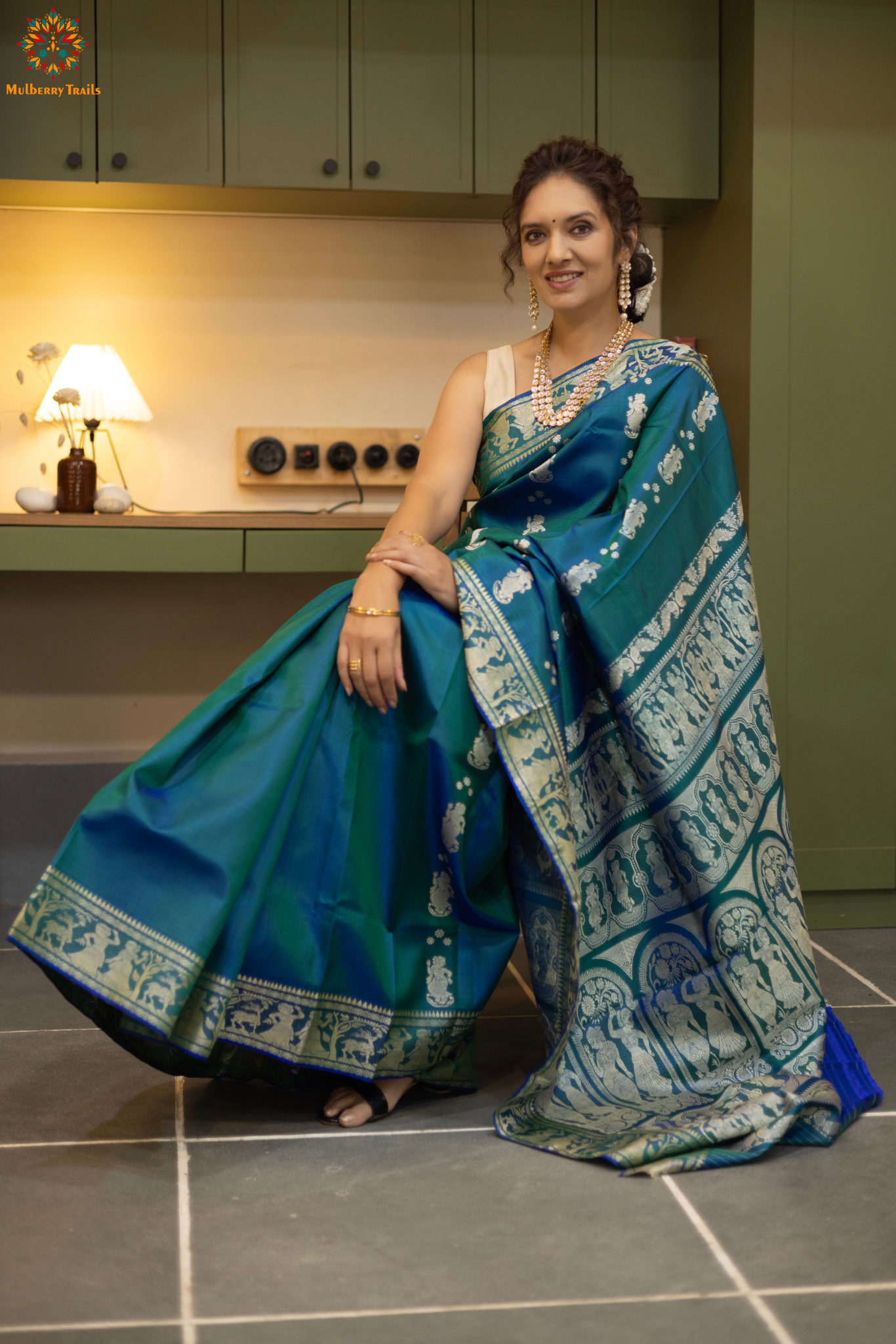 Woman wearing a traditional baluchari saree in a room with a desk and lamp. Woman in a Peacock blue and silver resham work saree standing indoors with a desk and lamp in the background.
Baluchari – Pure Silk Baluchari Saree
1. “Pure silk Baluchari saree with meenakari motif weave and Silver resham detailing for a regal look.”
2. “Silk Mark pure silk meenakari saree featuring intricate gold resham work motifs and rich texture.