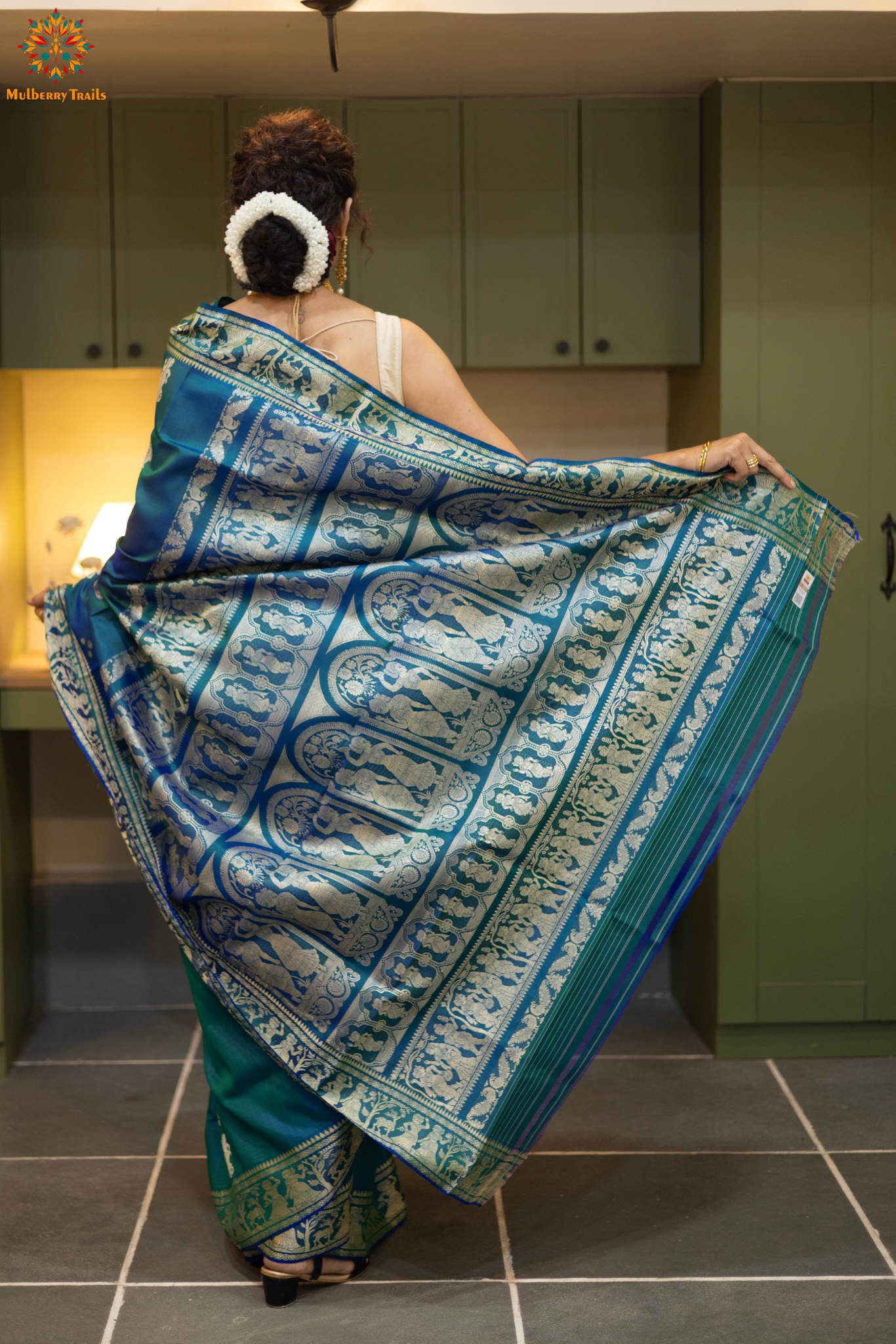 Woman wearing a traditional baluchari saree in a room with a desk and lamp. Woman in a Peacock blue and silver resham work saree standing indoors with a desk and lamp in the background.
Baluchari – Pure Silk Baluchari Saree
1. “Pure silk Baluchari saree with meenakari motif weave and Silver resham detailing for a regal look.”
2. “Silk Mark pure silk meenakari saree featuring intricate gold resham work motifs and rich texture.