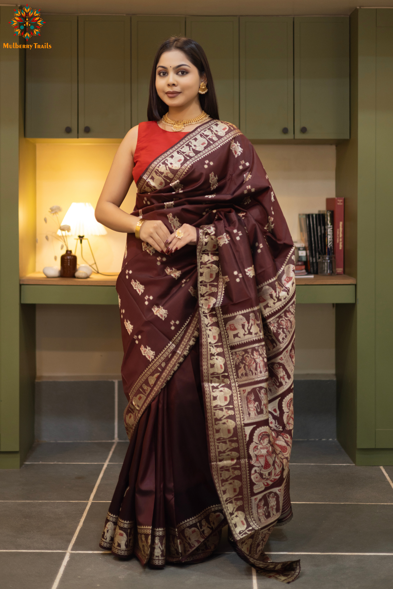 Woman in a Coffee brown and silver resham work saree standing indoors with a desk and lamp in the background.
Woman wearing a Coffee brown saree with a pattern in a elegant setting.
Baluchari – Pure Silk Meenakari Saree
1. “Pure silk Baluchari Meenakari saree with meenakari motif weave and Silver resham detailing for a regal look.”
2. “Silk Mark pure silk meenakari saree featuring intricate gold resham work motifs and rich texture.”
