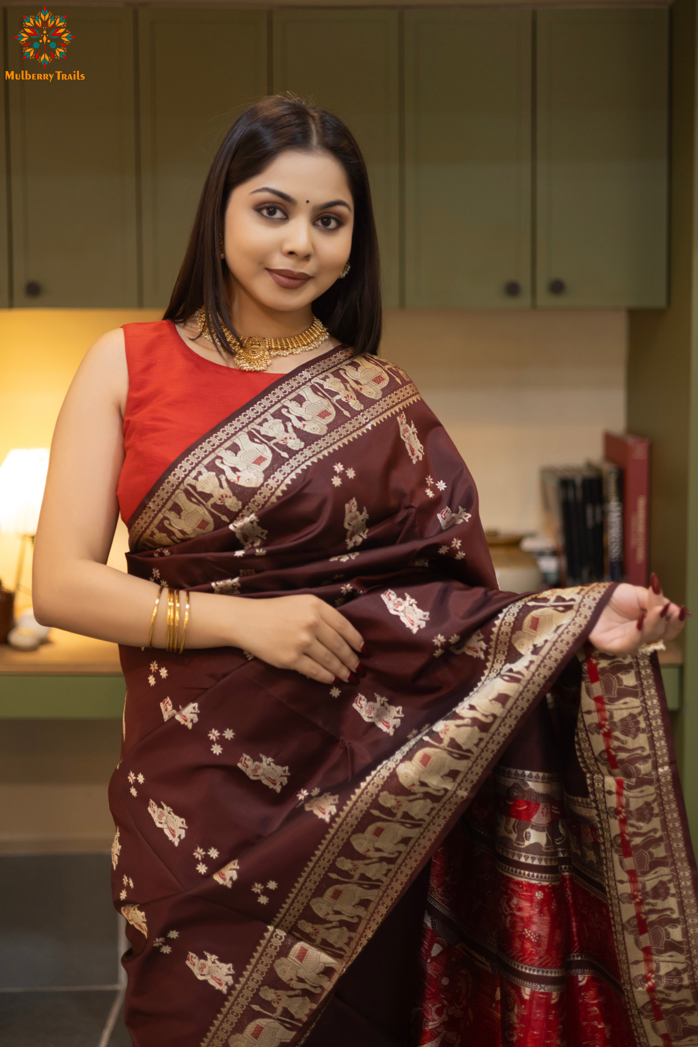 Woman in a Coffee brown and silver resham work saree standing indoors with a desk and lamp in the background.
Woman wearing a Coffee brown saree with a pattern in a elegant setting.
Baluchari – Pure Silk Meenakari Saree
1. “Pure silk Baluchari Meenakari saree with meenakari motif weave and Silver resham detailing for a regal look.”
2. “Silk Mark pure silk meenakari saree featuring intricate gold resham work motifs and rich texture.”