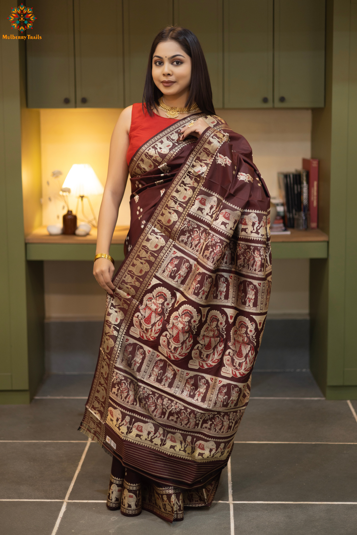 Woman in a Coffee brown and silver resham work saree standing indoors with a desk and lamp in the background.
Woman wearing a Coffee brown saree with a pattern in a elegant setting.
Baluchari – Pure Silk Meenakari Saree
1. “Pure silk Baluchari Meenakari saree with meenakari motif weave and Silver resham detailing for a regal look.”
2. “Silk Mark pure silk meenakari saree featuring intricate gold resham work motifs and rich texture.”