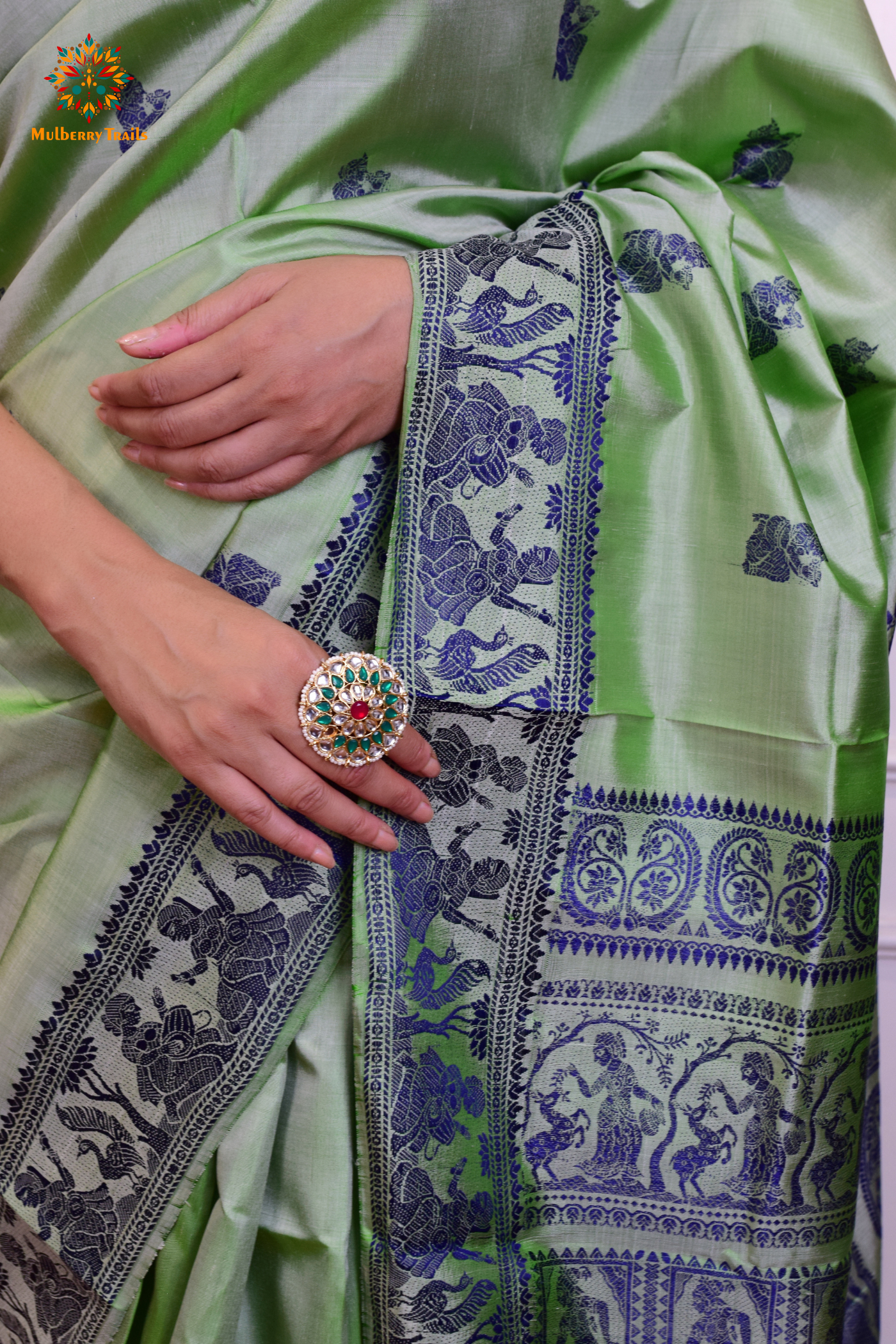 A woman wearing a Sage Green Baluchari Pure SIlk saree. purple baluchari silk , bengal silk saree with deer motif on pallu and ramayan, mahabharat motifs on pallu. This is a soft pure silk saree suitable for weddings, parties, festivities. suitable for Durga Puja shopping enthusiasts and diwali festival.