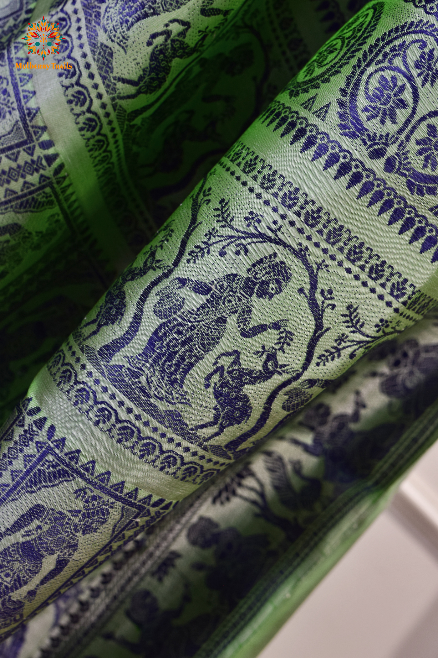 A woman wearing a Sage Green Baluchari Pure SIlk saree. purple baluchari silk , bengal silk saree with deer motif on pallu and ramayan, mahabharat motifs on pallu. This is a soft pure silk saree suitable for weddings, parties, festivities. suitable for Durga Puja shopping enthusiasts and diwali festival.