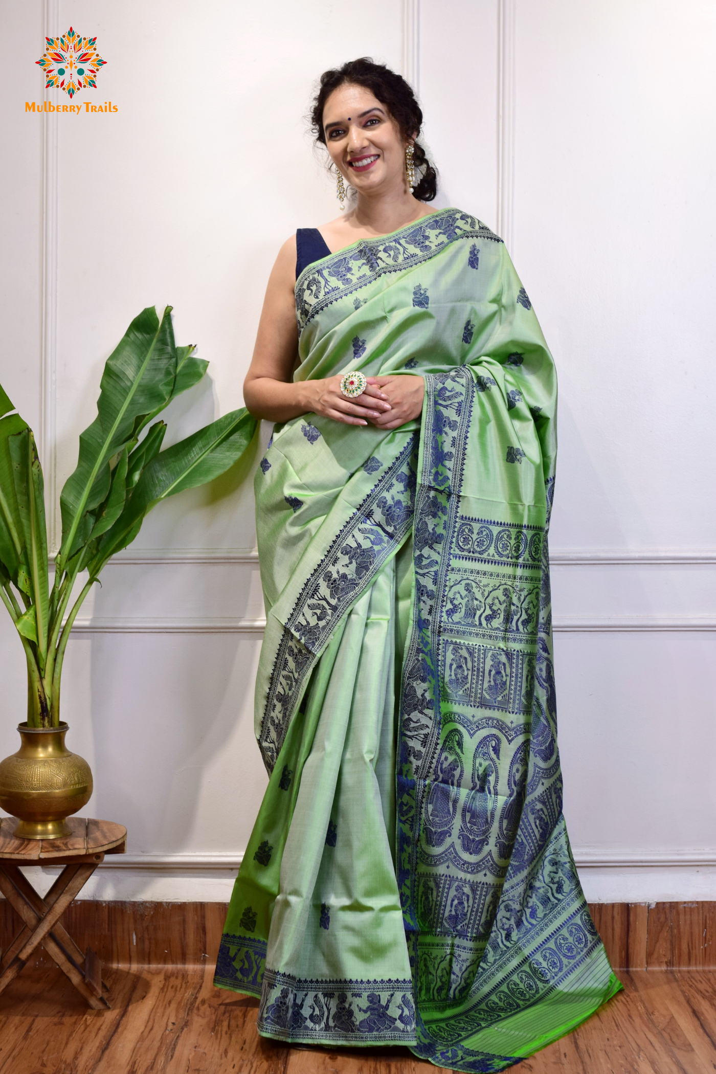 A woman wearing a Sage Green Baluchari Pure SIlk saree. purple baluchari silk , bengal silk saree with deer motif on pallu and ramayan, mahabharat motifs on pallu. This is a soft pure silk saree suitable for weddings, parties, festivities. suitable for Durga Puja shopping enthusiasts and diwali festival.