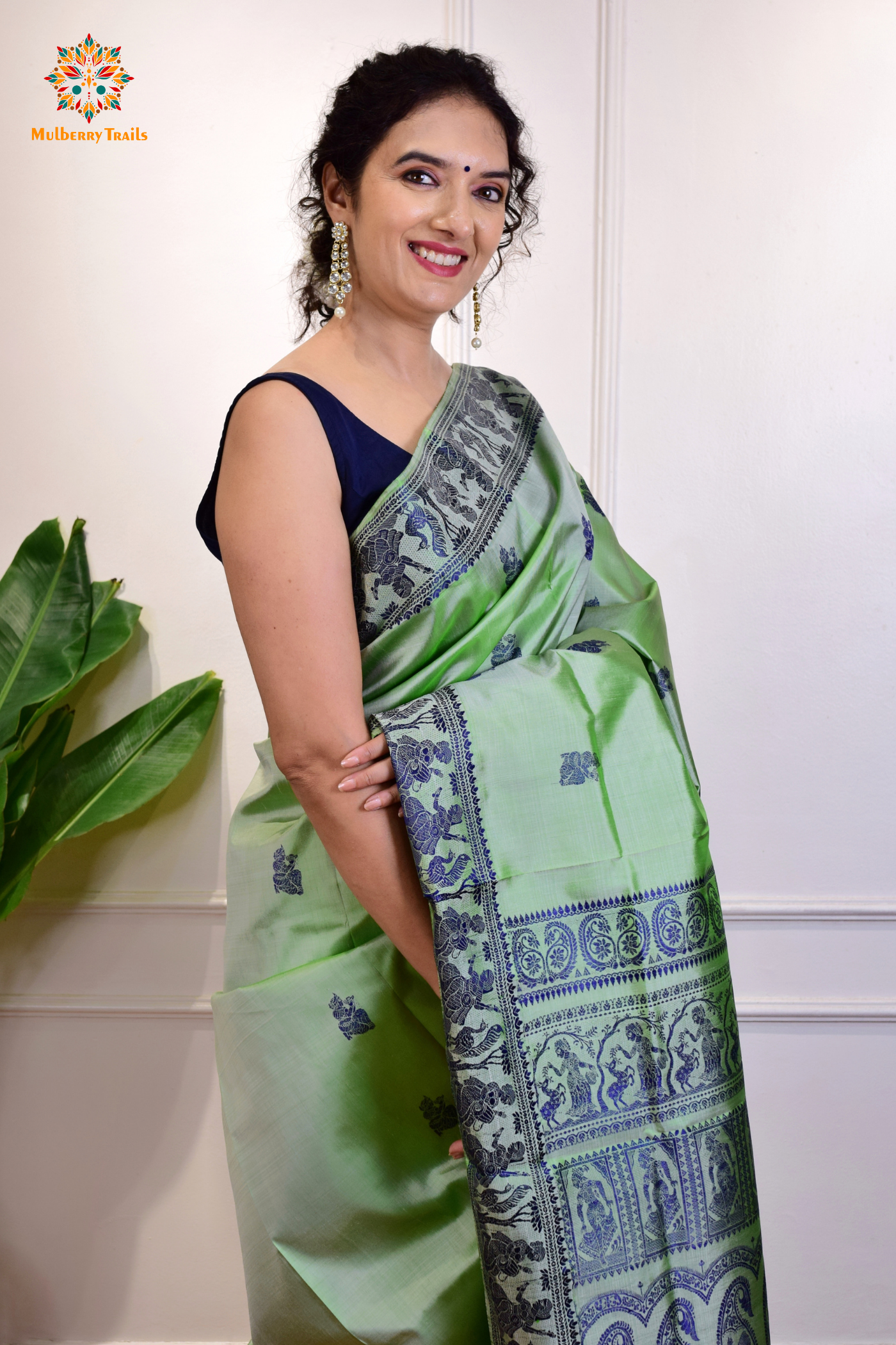 A woman wearing a Sage Green Baluchari Pure SIlk saree. purple baluchari silk , bengal silk saree with deer motif on pallu and ramayan, mahabharat motifs on pallu. This is a soft pure silk saree suitable for weddings, parties, festivities. suitable for Durga Puja shopping enthusiasts and diwali festival.