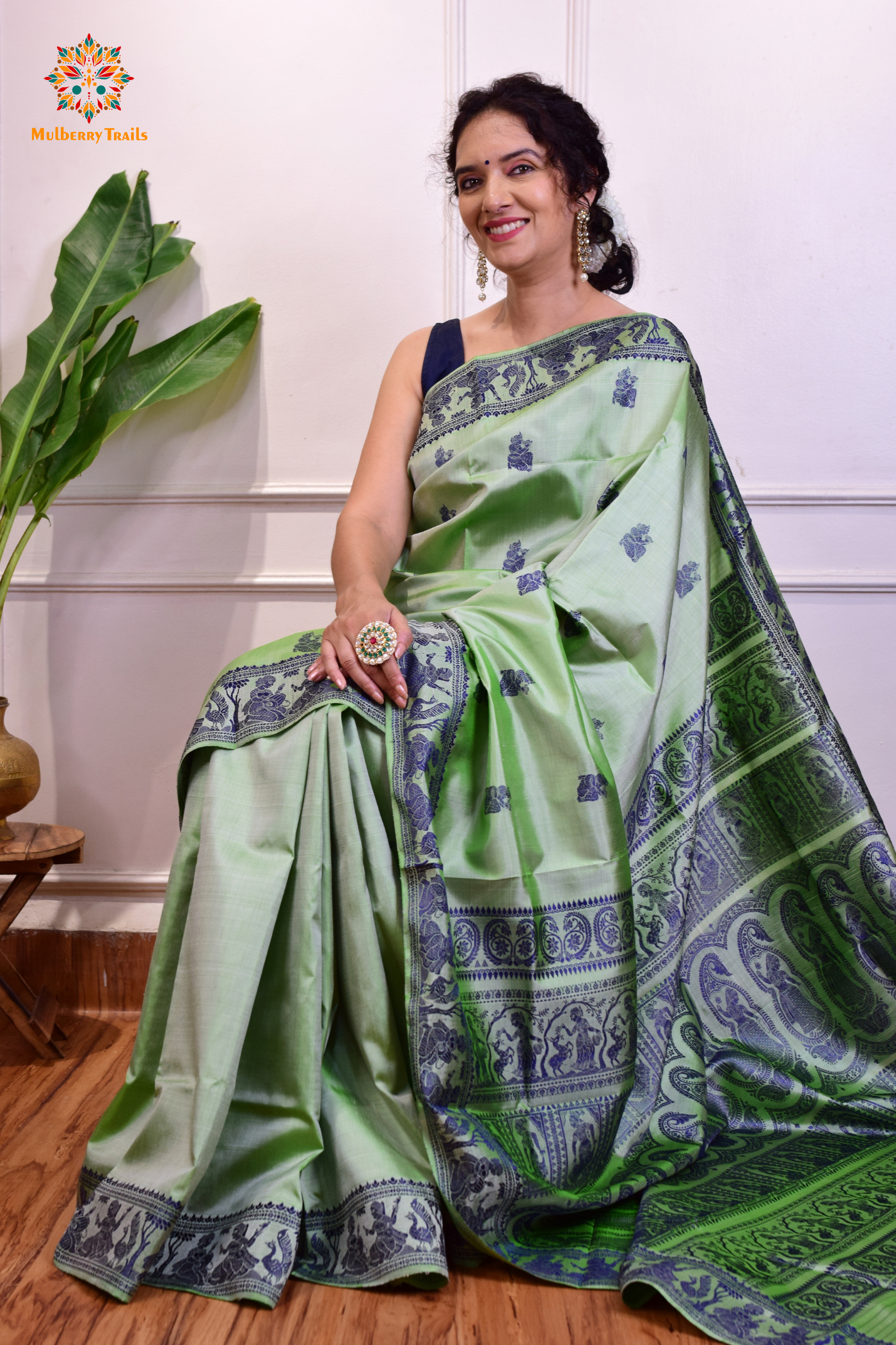 A woman wearing a Sage Green Baluchari Pure SIlk saree. purple baluchari silk , bengal silk saree with deer motif on pallu and ramayan, mahabharat motifs on pallu. This is a soft pure silk saree suitable for weddings, parties, festivities. suitable for Durga Puja shopping enthusiasts and diwali festival.