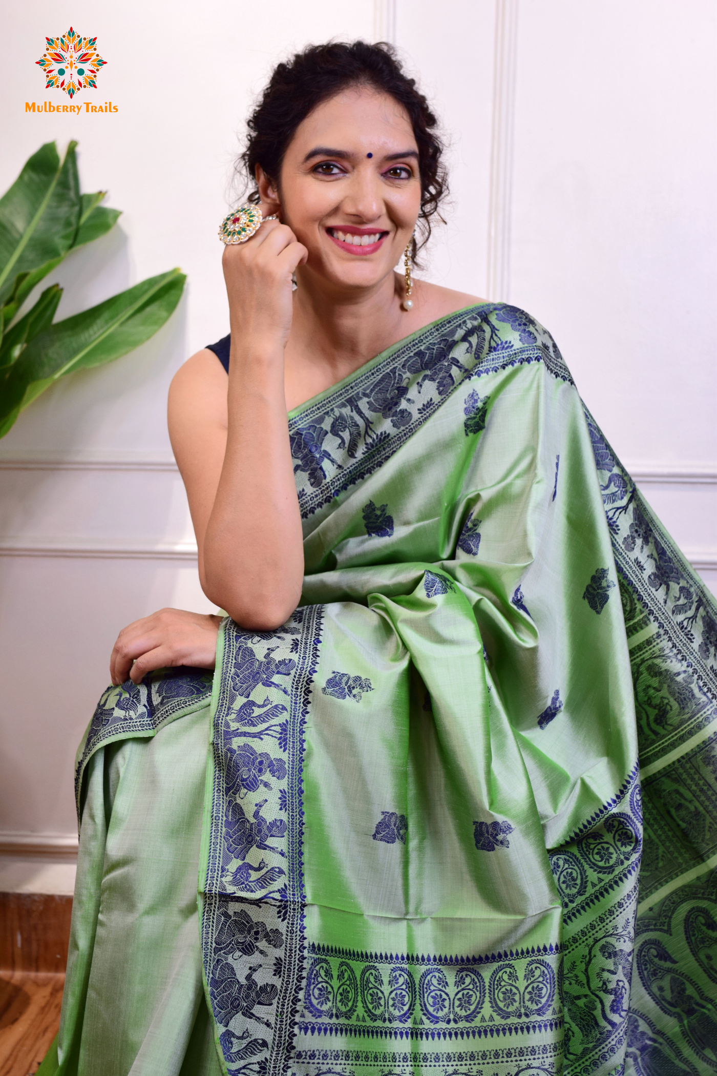A woman wearing a Sage Green Baluchari Pure SIlk saree. purple baluchari silk , bengal silk saree with deer motif on pallu and ramayan, mahabharat motifs on pallu. This is a soft pure silk saree suitable for weddings, parties, festivities. suitable for Durga Puja shopping enthusiasts and diwali festival.