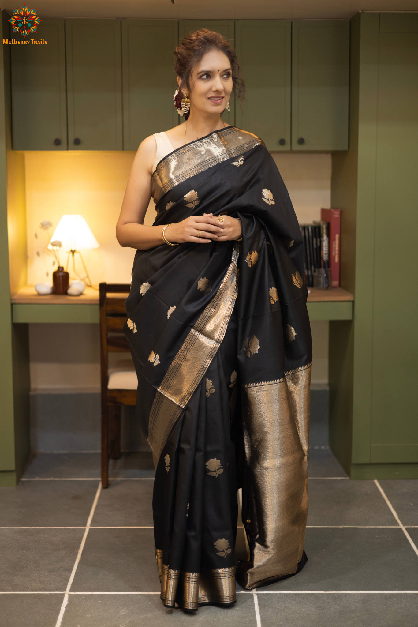 Woman in a black saree with gold patterns sitting indoor. Woman wearing a traditional baluchari saree in a room with a desk and lamp. Woman in a carrot red and silver resham work saree standing indoors with a desk and lamp in the background.
Baluchari – Pure Silk Baluchari Saree
1. “Pure silk Baluchari saree with temple motif weave and Silver resham detailing for a regal look.”
2. “Silk Mark pure silk saree featuring intricate gold resham work motifs and rich texture.