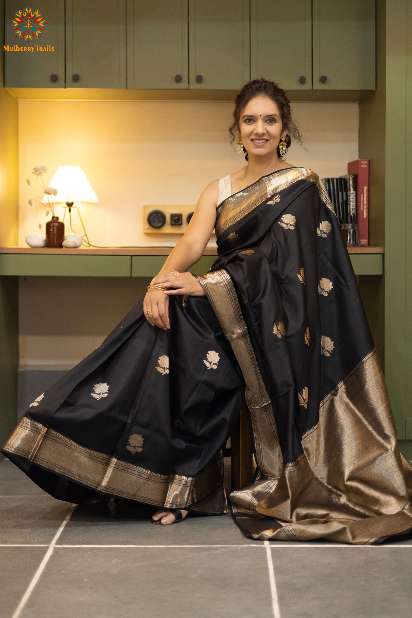 Woman in a black saree with gold patterns sitting indoor. Woman wearing a traditional baluchari saree in a room with a desk and lamp. Woman in a carrot red and silver resham work saree standing indoors with a desk and lamp in the background.
Baluchari – Pure Silk Baluchari Saree
1. “Pure silk Baluchari saree with temple motif weave and Silver resham detailing for a regal look.”
2. “Silk Mark pure silk saree featuring intricate gold resham work motifs and rich texture.