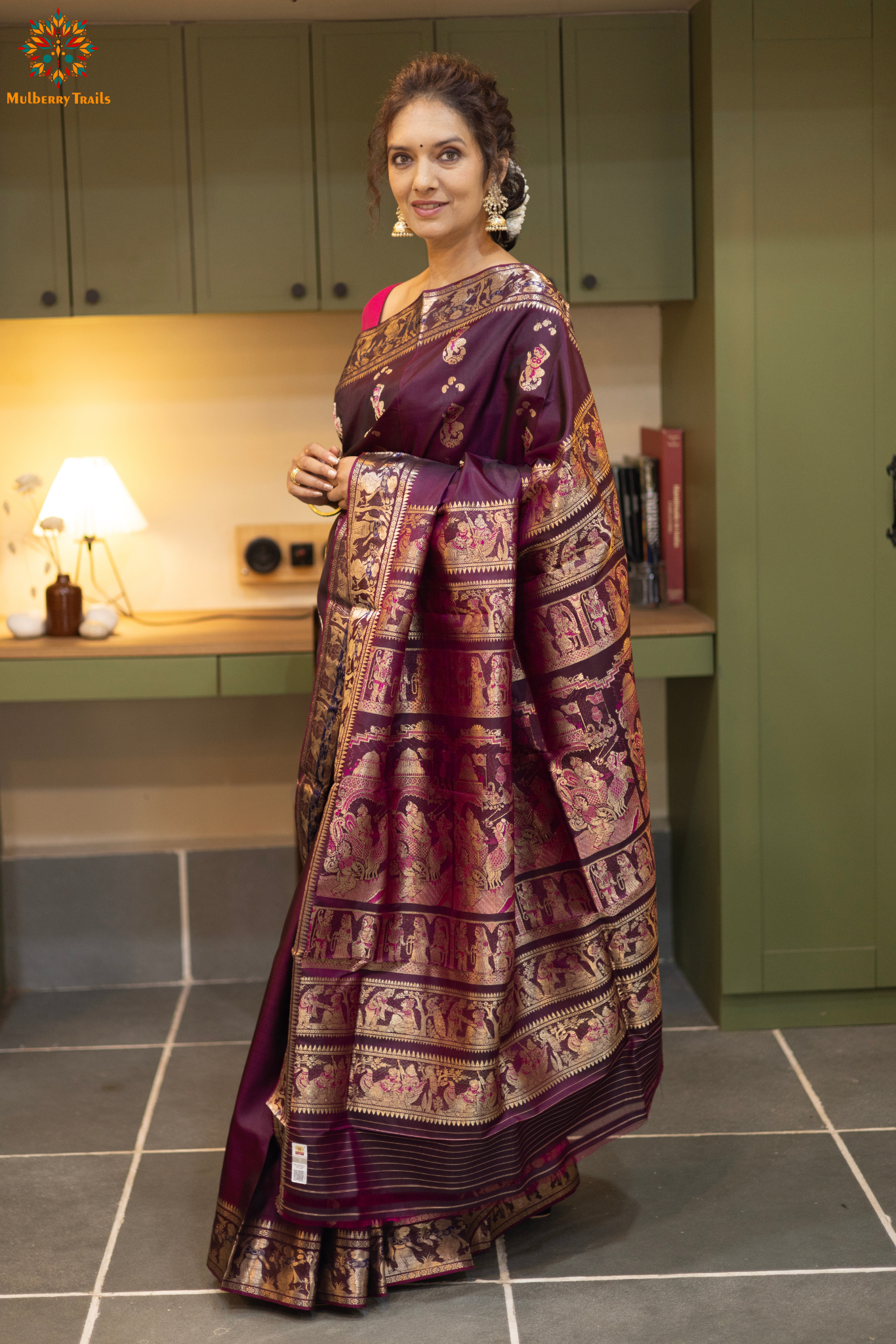 Woman wearing a purple saree with a pattern in a room. Woman in a wine saree standing in a elegant setting.
Swarnachari – Pure Silk Meenakari Saree
1. “Pure silk Swarnachari saree with meenakari motif weave and gold copper zari detailing for a regal look.”
2. “Silk Mark pure silk meenakari saree featuring intricate copper gold zari motifs and rich texture.”
Woman wearing a wine color swarnachari saree in a room with a desk and lamp.