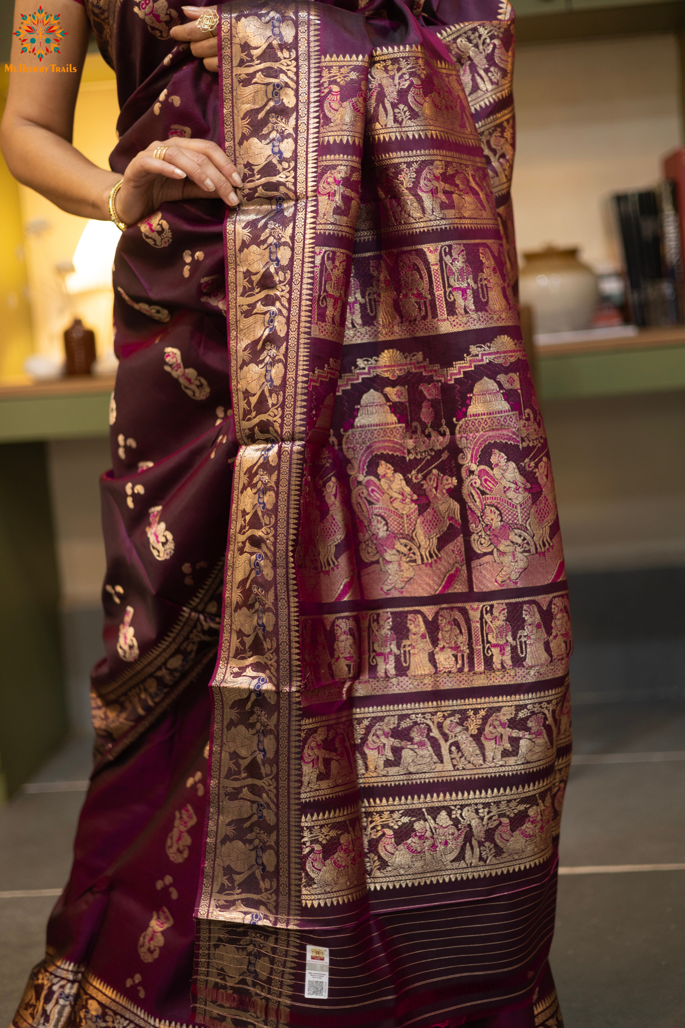 Woman wearing a purple saree with a pattern in a room. Woman in a wine saree standing in a elegant setting.
Swarnachari – Pure Silk Meenakari Saree
1. “Pure silk Swarnachari saree with meenakari motif weave and gold copper zari detailing for a regal look.”
2. “Silk Mark pure silk meenakari saree featuring intricate copper gold zari motifs and rich texture.”
Woman wearing a wine color swarnachari saree in a room with a desk and lamp.