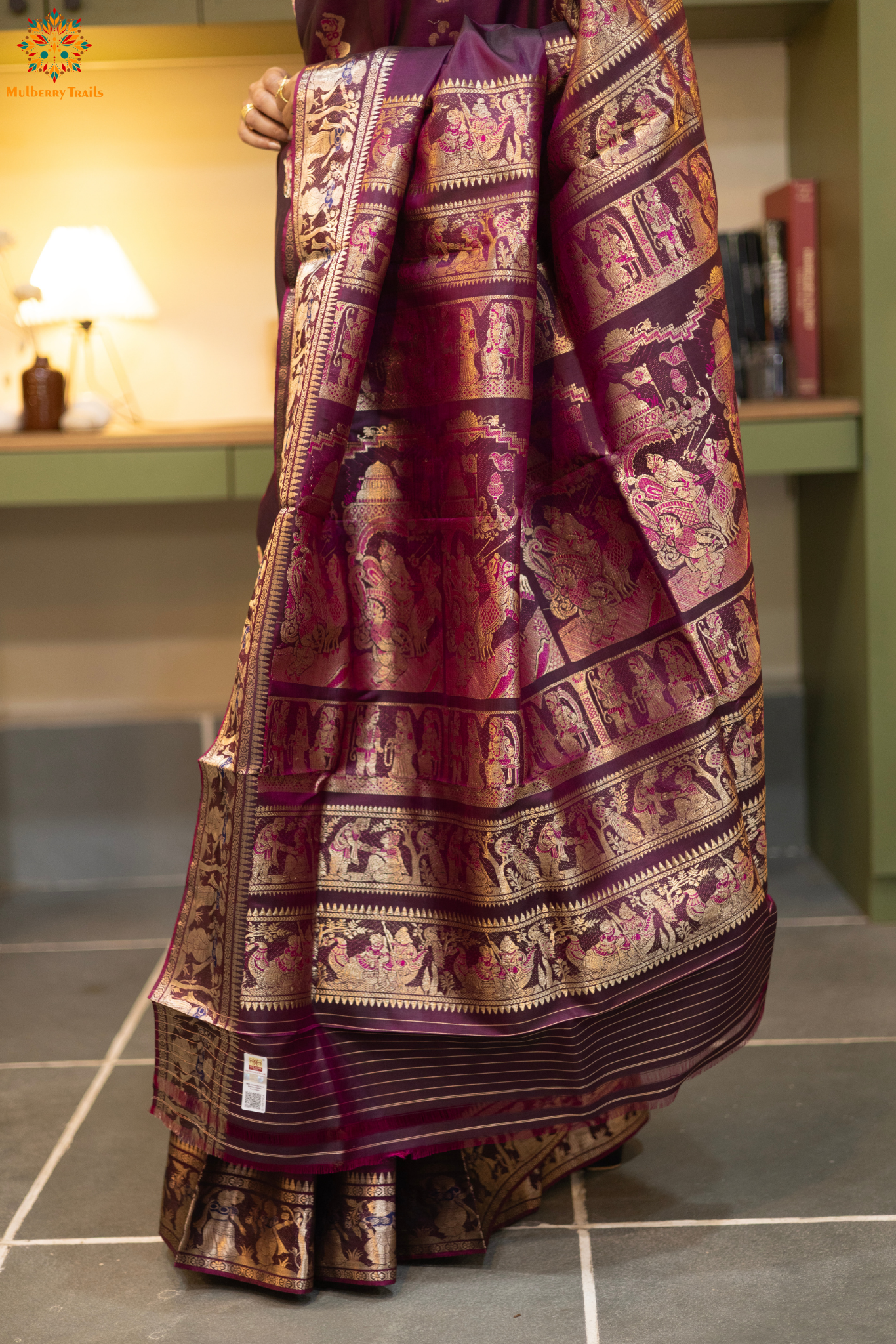 Woman wearing a purple saree with a pattern in a room. Woman in a wine saree standing in a elegant setting.
Swarnachari – Pure Silk Meenakari Saree
1. “Pure silk Swarnachari saree with meenakari motif weave and gold copper zari detailing for a regal look.”
2. “Silk Mark pure silk meenakari saree featuring intricate copper gold zari motifs and rich texture.”
Woman wearing a wine color swarnachari saree in a room with a desk and lamp.