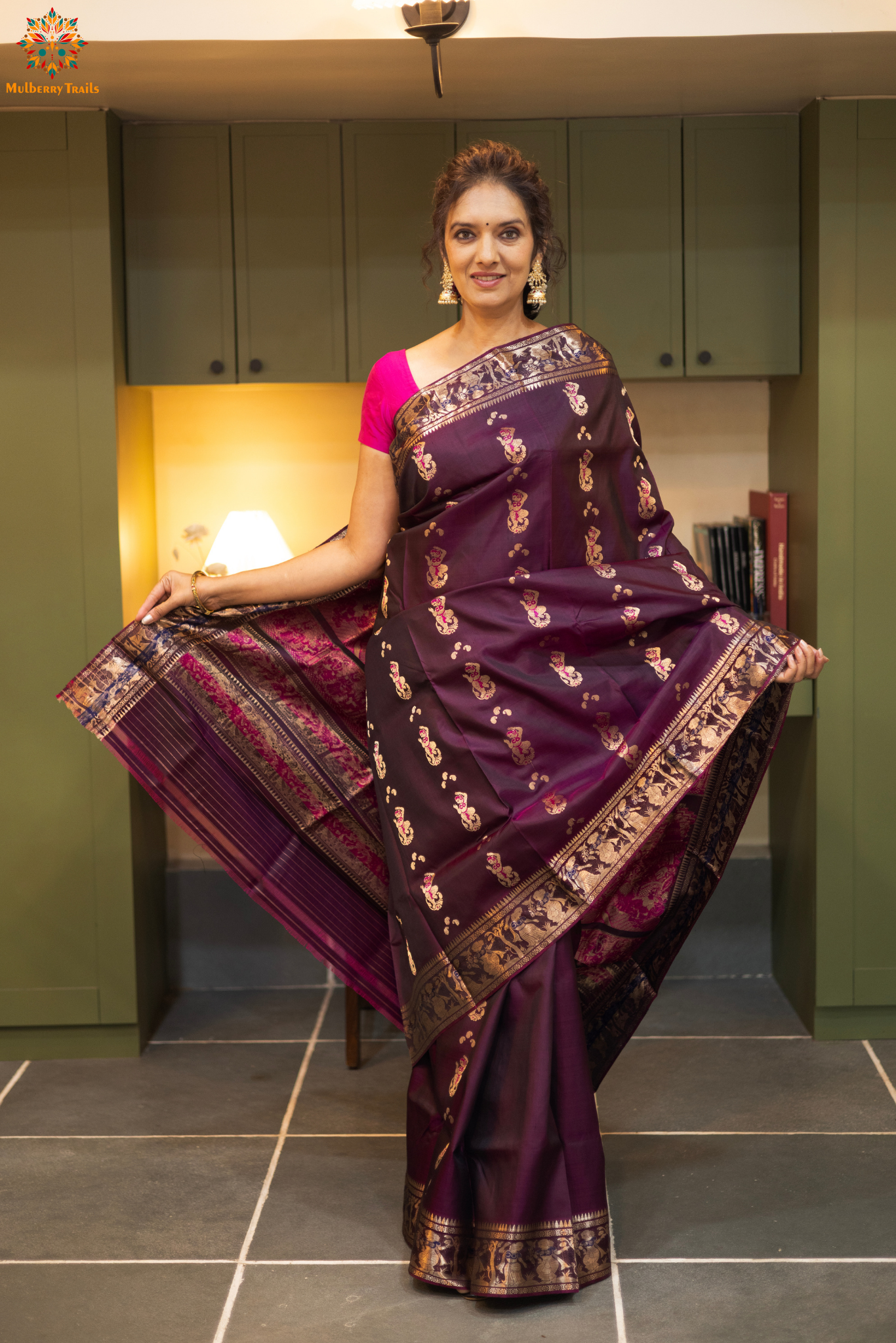 Woman wearing a purple saree with a pattern in a room. Woman in a wine saree standing in a elegant setting.
Swarnachari – Pure Silk Meenakari Saree
1. “Pure silk Swarnachari saree with meenakari motif weave and gold copper zari detailing for a regal look.”
2. “Silk Mark pure silk meenakari saree featuring intricate copper gold zari motifs and rich texture.”
Woman wearing a wine color swarnachari saree in a room with a desk and lamp.