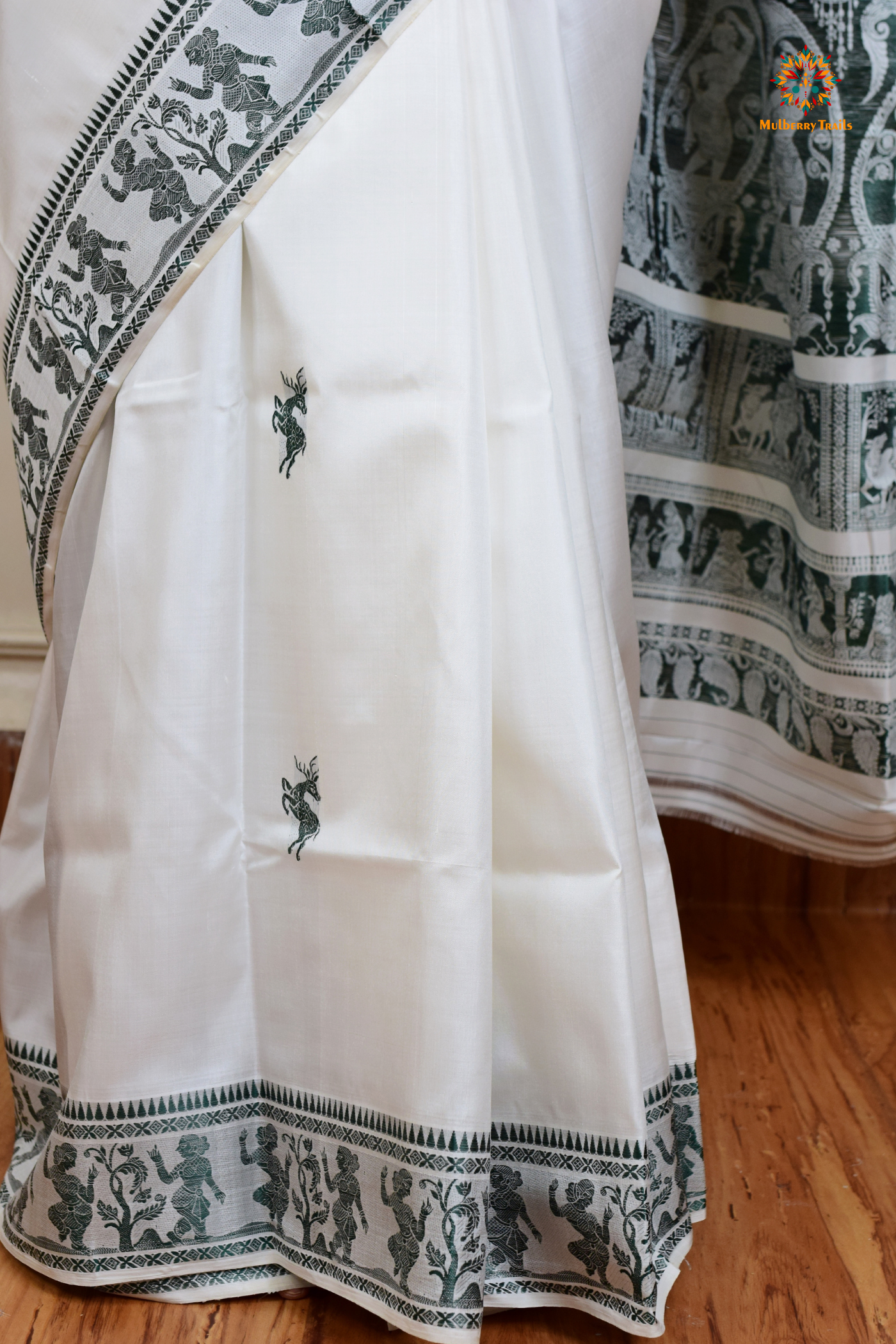 A woman wearing a White Baluchari Pure SIlk saree. White baluchari silk , bengal silk saree with deer motif on pallu and ramayan, mahabharat motifs on pallu. This is a soft pure silk saree suitable for weddings, parties, festivities. suitable for Durga Puja shopping enthusiasts and diwali festival.