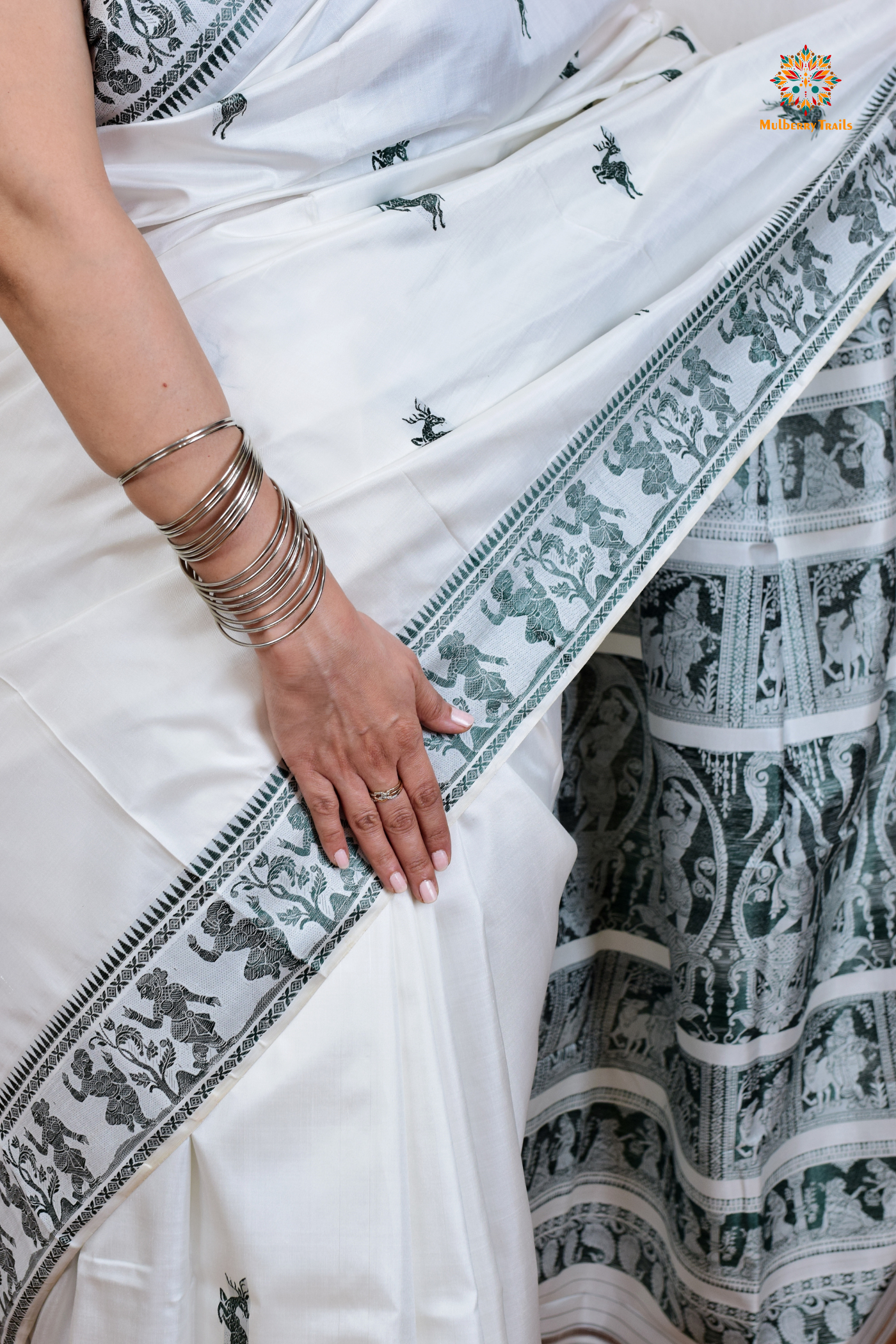 A woman wearing a White Baluchari Pure SIlk saree. White baluchari silk , bengal silk saree with deer motif on pallu and ramayan, mahabharat motifs on pallu. This is a soft pure silk saree suitable for weddings, parties, festivities. suitable for Durga Puja shopping enthusiasts and diwali festival.