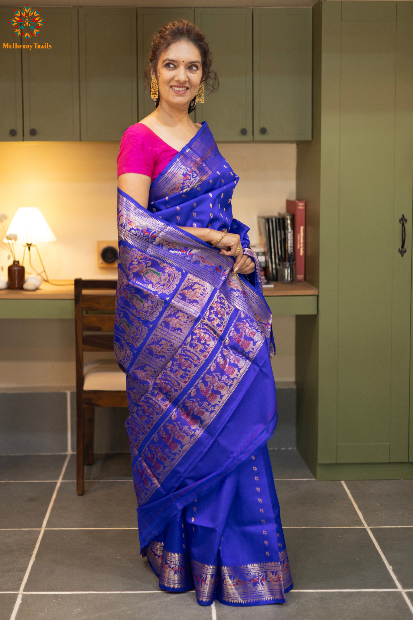 Woman wearing a blue saree with a pink blouse in an indoor setting.
Swarnachari – Pure Silk Hazarbutta Saree
1. “Pure silk Swarnachari saree with hazarbutta thousand-motif weave and copper zari detailing for a regal look.”
2. “Silk Mark pure silk hazarbutta saree featuring intricate copper zari motifs and rich texture.”
Woman wearing a black and copper zari saree in a room with a desk and lamp.