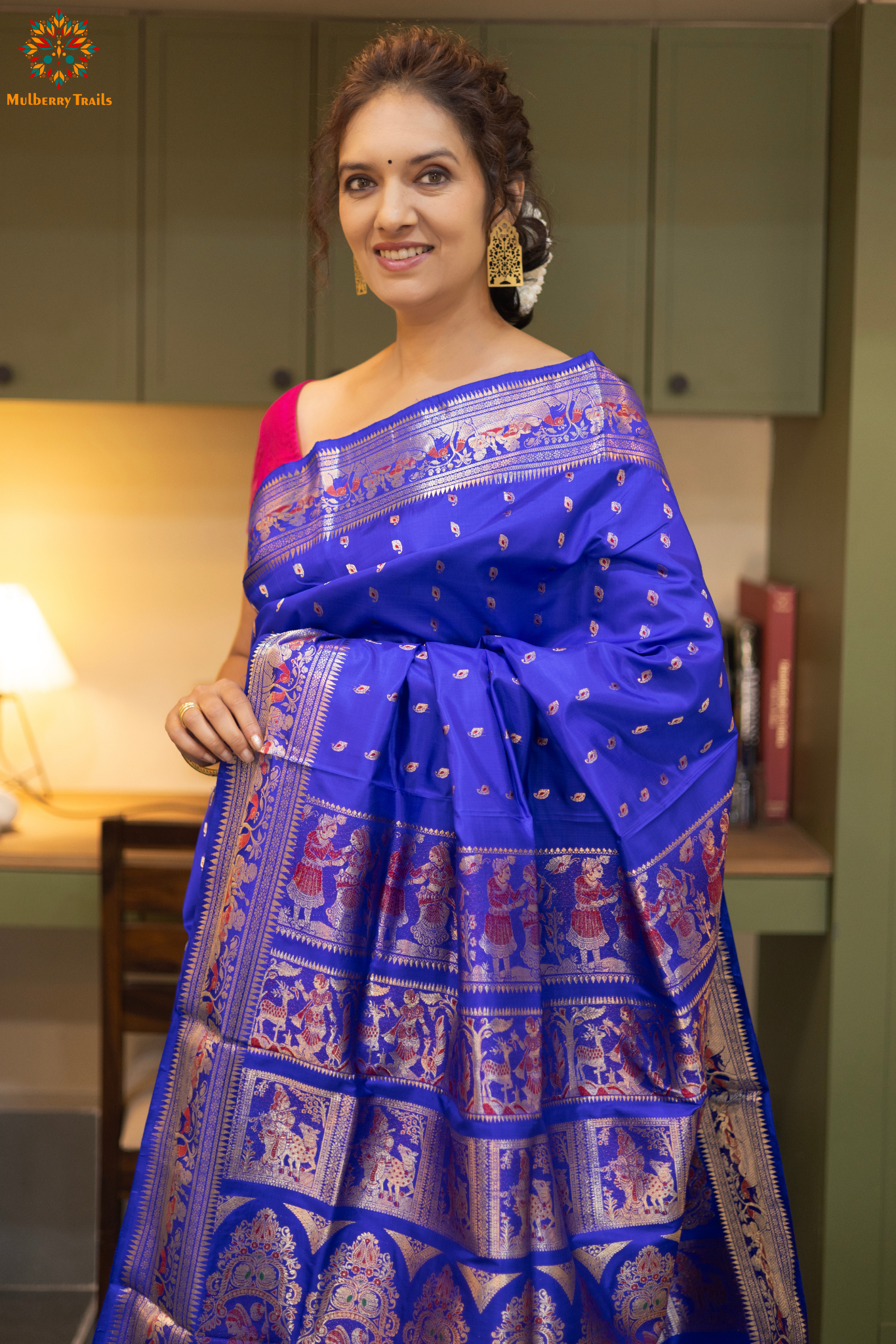 Swarnachari – Pure Silk Hazarbutta Saree
1. “Pure silk Swarnachari saree with hazarbutta thousand-motif weave and copper zari detailing for a regal look.”
2. “Silk Mark pure silk hazarbutta saree featuring intricate copper zari motifs and rich texture.”
Woman wearing a black and copper zari saree in a room with a desk and lamp.