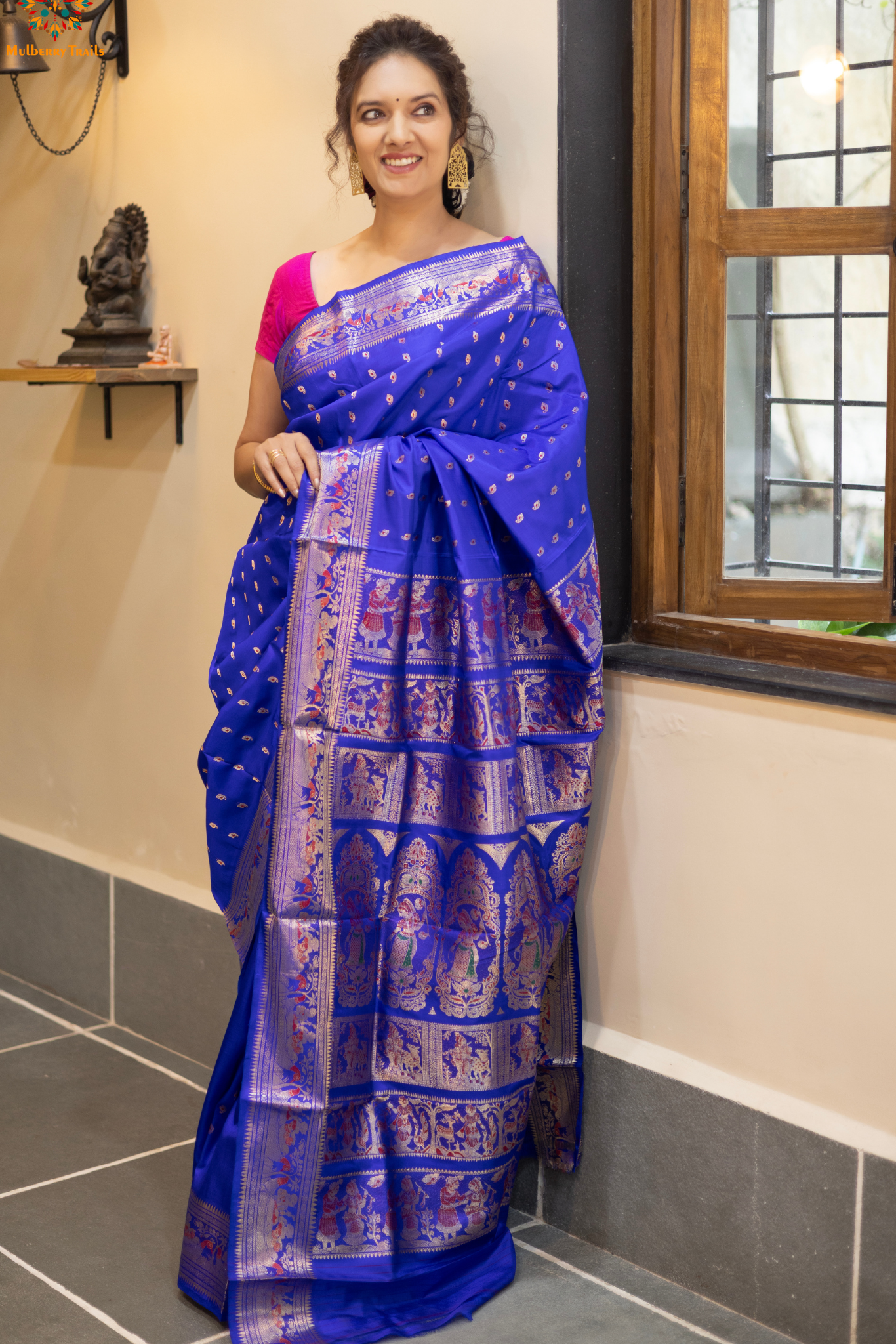 Swarnachari – Pure Silk Hazarbutta Saree
1. “Pure silk Swarnachari saree with hazarbutta thousand-motif weave and copper zari detailing for a regal look.”
2. “Silk Mark pure silk hazarbutta saree featuring intricate copper zari motifs and rich texture.”
Woman wearing a black and copper zari saree in a room with a desk and lamp.