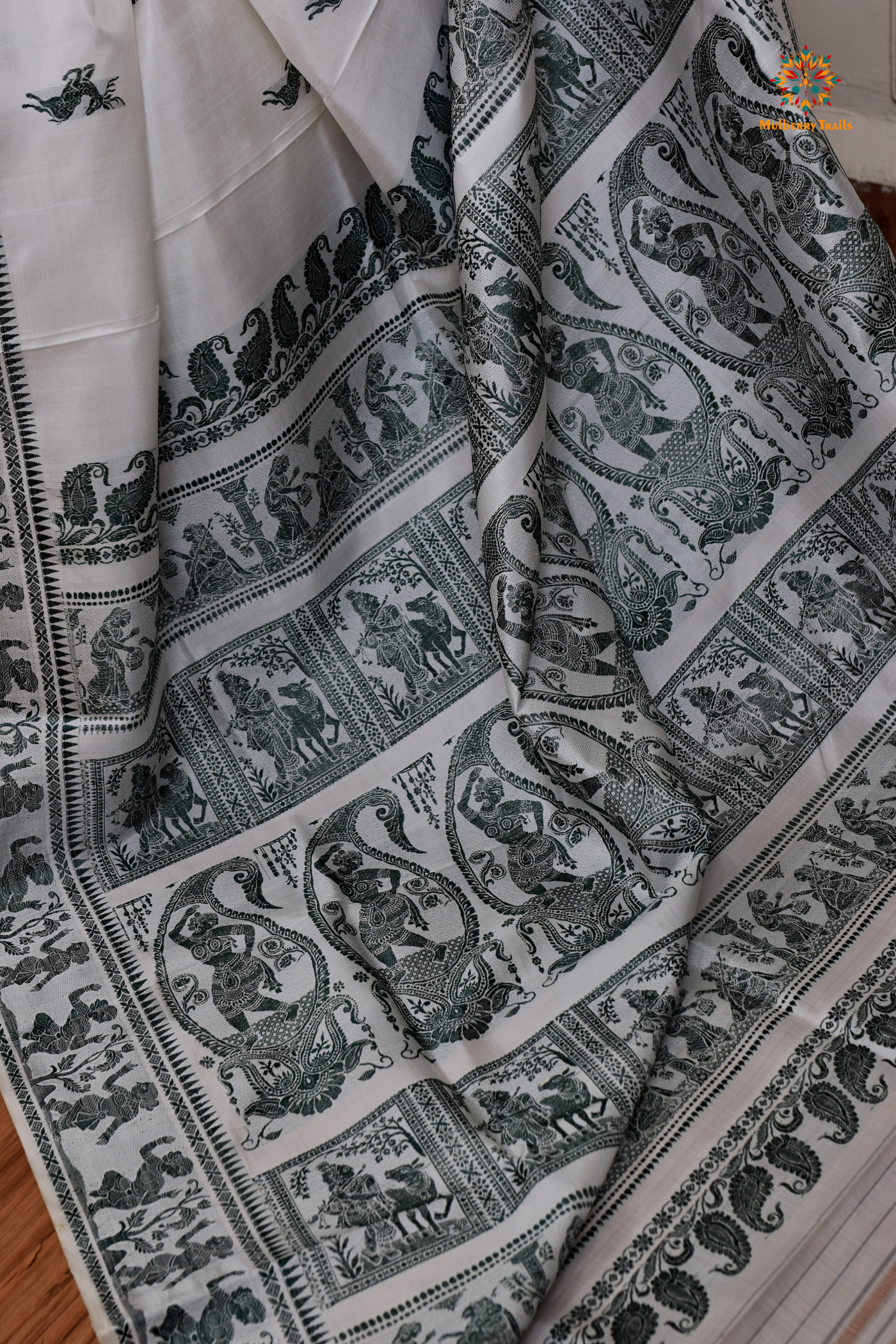 A woman wearing a White Baluchari Pure SIlk saree. White baluchari silk , bengal silk saree with deer motif on pallu and ramayan, mahabharat motifs on pallu. This is a soft pure silk saree suitable for weddings, parties, festivities. suitable for Durga Puja shopping enthusiasts and diwali festival.