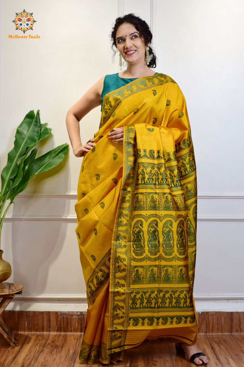 A woman wearing a Yellow Baluchari Pure SIlk saree. purple baluchari silk , bengal silk saree with deer motif on pallu and ramayan, mahabharat motifs on pallu. This is a soft pure silk saree suitable for weddings, parties, festivities. suitable for Durga Puja shopping enthusiasts and diwali festival. 