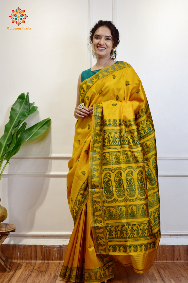 A woman wearing a Yellow Baluchari Pure SIlk saree. purple baluchari silk , bengal silk saree with deer motif on pallu and ramayan, mahabharat motifs on pallu. This is a soft pure silk saree suitable for weddings, parties, festivities. suitable for Durga Puja shopping enthusiasts and diwali festival. 