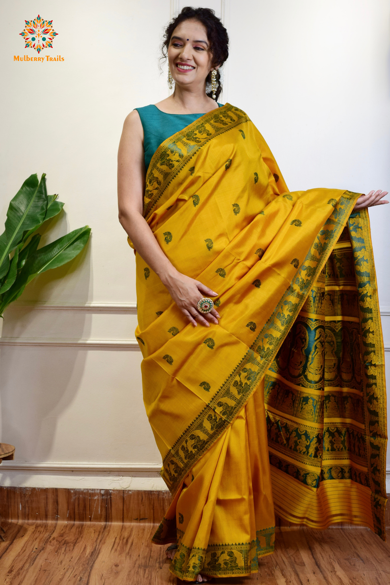 A woman wearing a Yellow Baluchari Pure SIlk saree. purple baluchari silk , bengal silk saree with deer motif on pallu and ramayan, mahabharat motifs on pallu. This is a soft pure silk saree suitable for weddings, parties, festivities. suitable for Durga Puja shopping enthusiasts and diwali festival. 