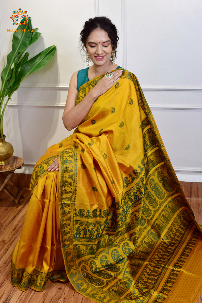 A woman wearing a Yellow Baluchari Pure SIlk saree. purple baluchari silk , bengal silk saree with deer motif on pallu and ramayan, mahabharat motifs on pallu. This is a soft pure silk saree suitable for weddings, parties, festivities. suitable for Durga Puja shopping enthusiasts and diwali festival. 