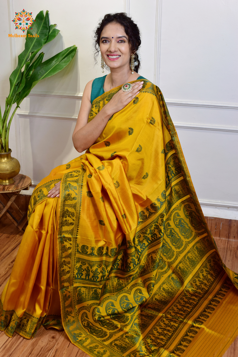 A woman wearing a Yellow Baluchari Pure SIlk saree. purple baluchari silk , bengal silk saree with deer motif on pallu and ramayan, mahabharat motifs on pallu. This is a soft pure silk saree suitable for weddings, parties, festivities. suitable for Durga Puja shopping enthusiasts and diwali festival. 