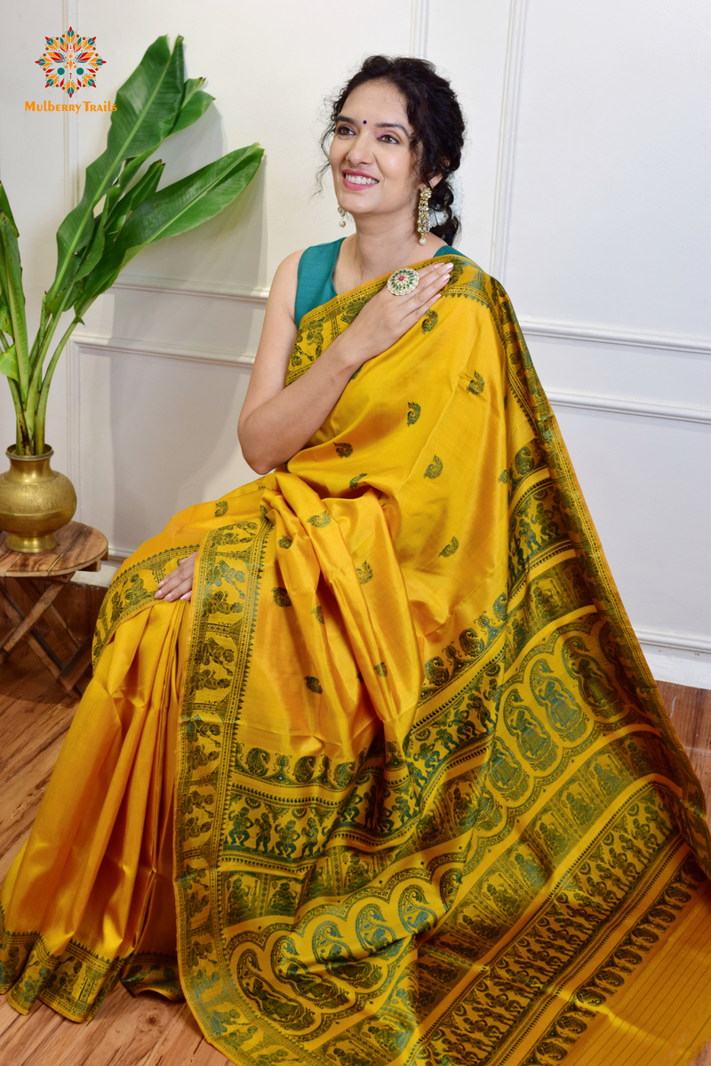 A woman wearing a Yellow Baluchari Pure SIlk saree. purple baluchari silk , bengal silk saree with deer motif on pallu and ramayan, mahabharat motifs on pallu. This is a soft pure silk saree suitable for weddings, parties, festivities. suitable for Durga Puja shopping enthusiasts and diwali festival. 