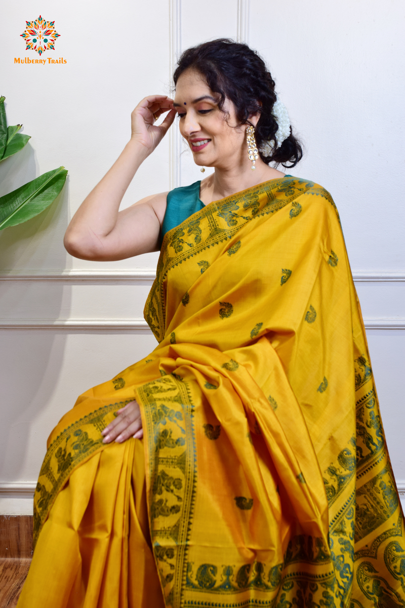 A woman wearing a Yellow Baluchari Pure SIlk saree. purple baluchari silk , bengal silk saree with deer motif on pallu and ramayan, mahabharat motifs on pallu. This is a soft pure silk saree suitable for weddings, parties, festivities. suitable for Durga Puja shopping enthusiasts and diwali festival. 