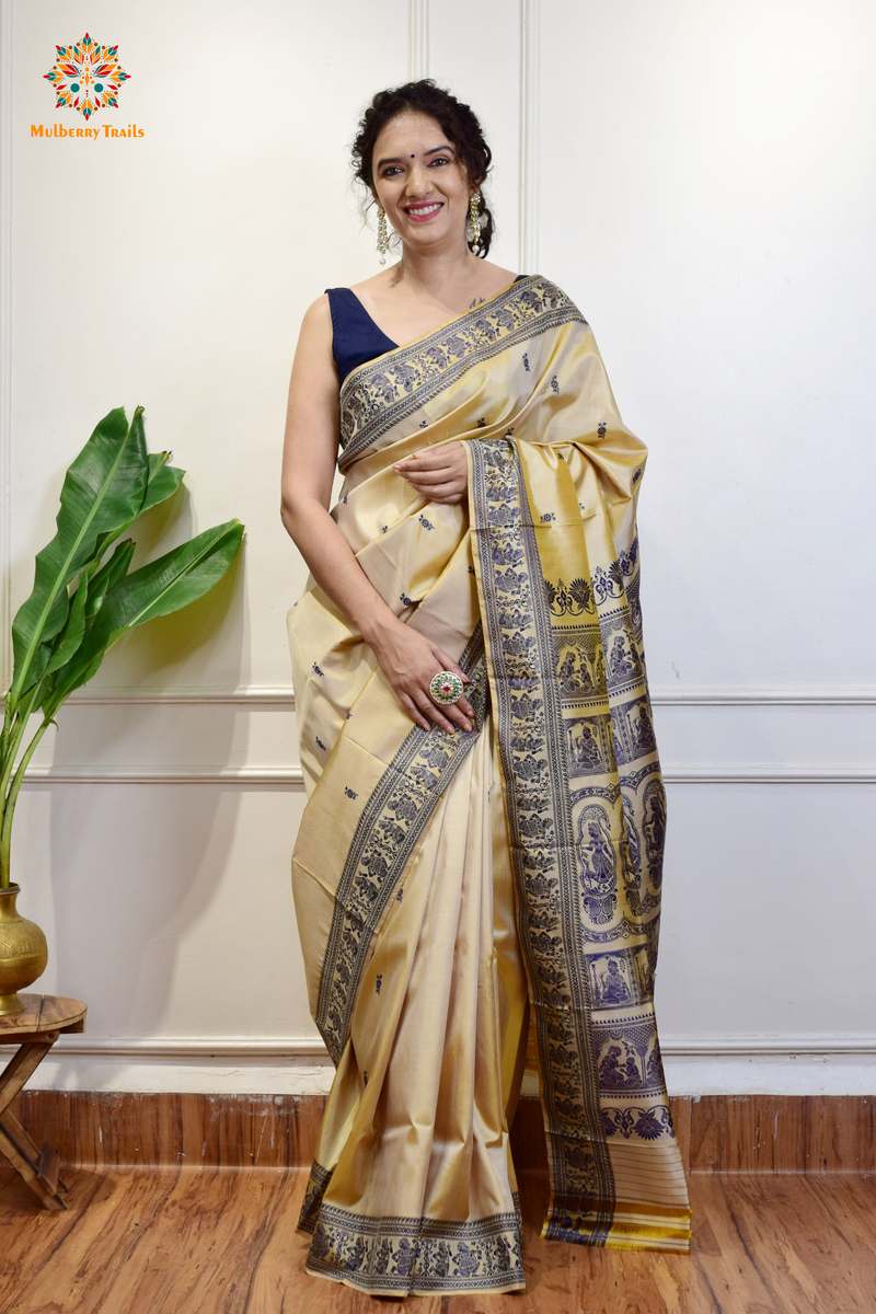 A woman wearing a Beige Baluchari Pure SIlk saree. purple baluchari silk , bengal silk saree with deer motif on pallu and ramayan, mahabharat motifs on pallu. This is a soft pure silk saree suitable for weddings, parties, festivities. suitable for Durga Puja shopping enthusiasts and diwali festival. 