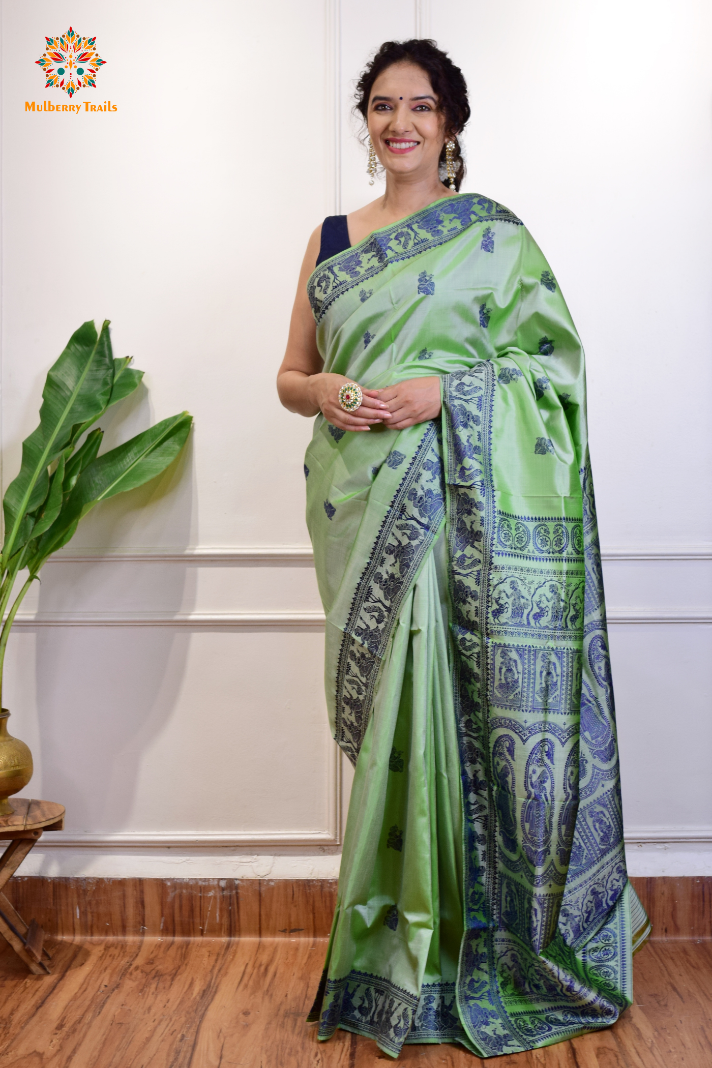 A woman wearing a Sage Green Baluchari Pure SIlk saree. purple baluchari silk , bengal silk saree with deer motif on pallu and ramayan, mahabharat motifs on pallu. This is a soft pure silk saree suitable for weddings, parties, festivities. suitable for Durga Puja shopping enthusiasts and diwali festival. 