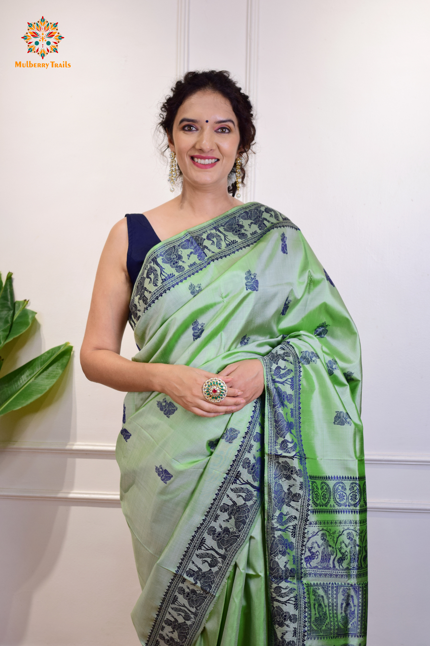 A woman wearing a Sage Green Baluchari Pure SIlk saree. purple baluchari silk , bengal silk saree with deer motif on pallu and ramayan, mahabharat motifs on pallu. This is a soft pure silk saree suitable for weddings, parties, festivities. suitable for Durga Puja shopping enthusiasts and diwali festival. 