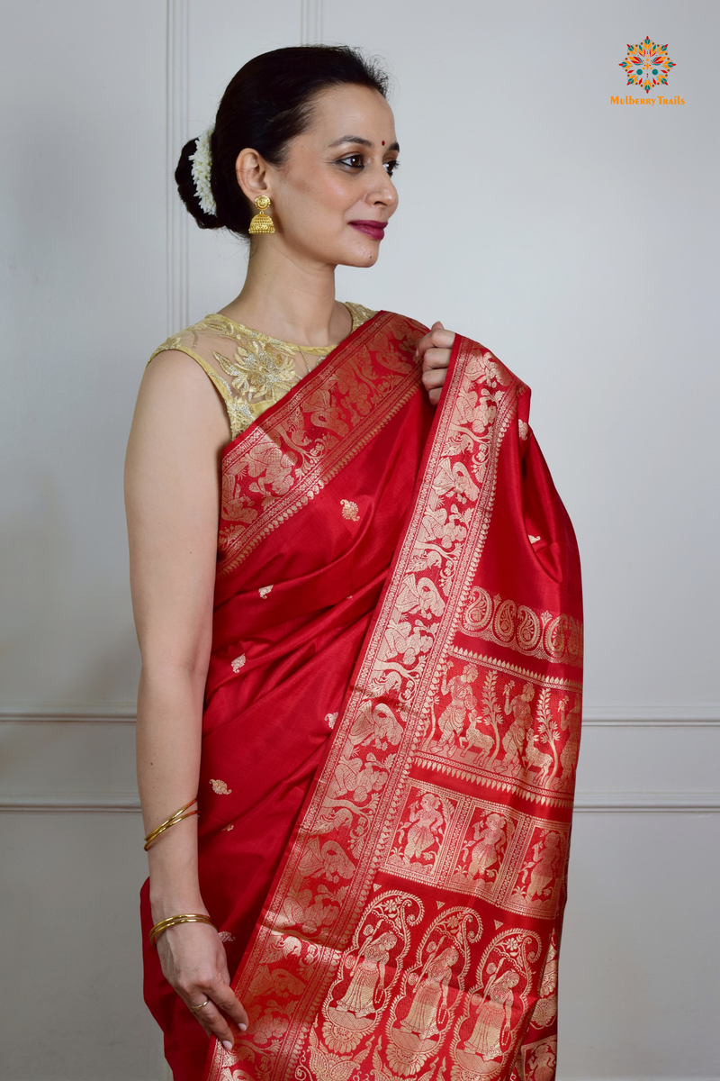 A woman wearing a Red Baluchari Pure SIlk saree. Red baluchari silk , bengal silk saree with deer motif on pallu and ramayan, mahabharat motifs on pallu. This is a soft pure silk saree suitable for weddings, parties, festivities. suitable for Durga Puja shopping enthusiasts and diwali festival. 