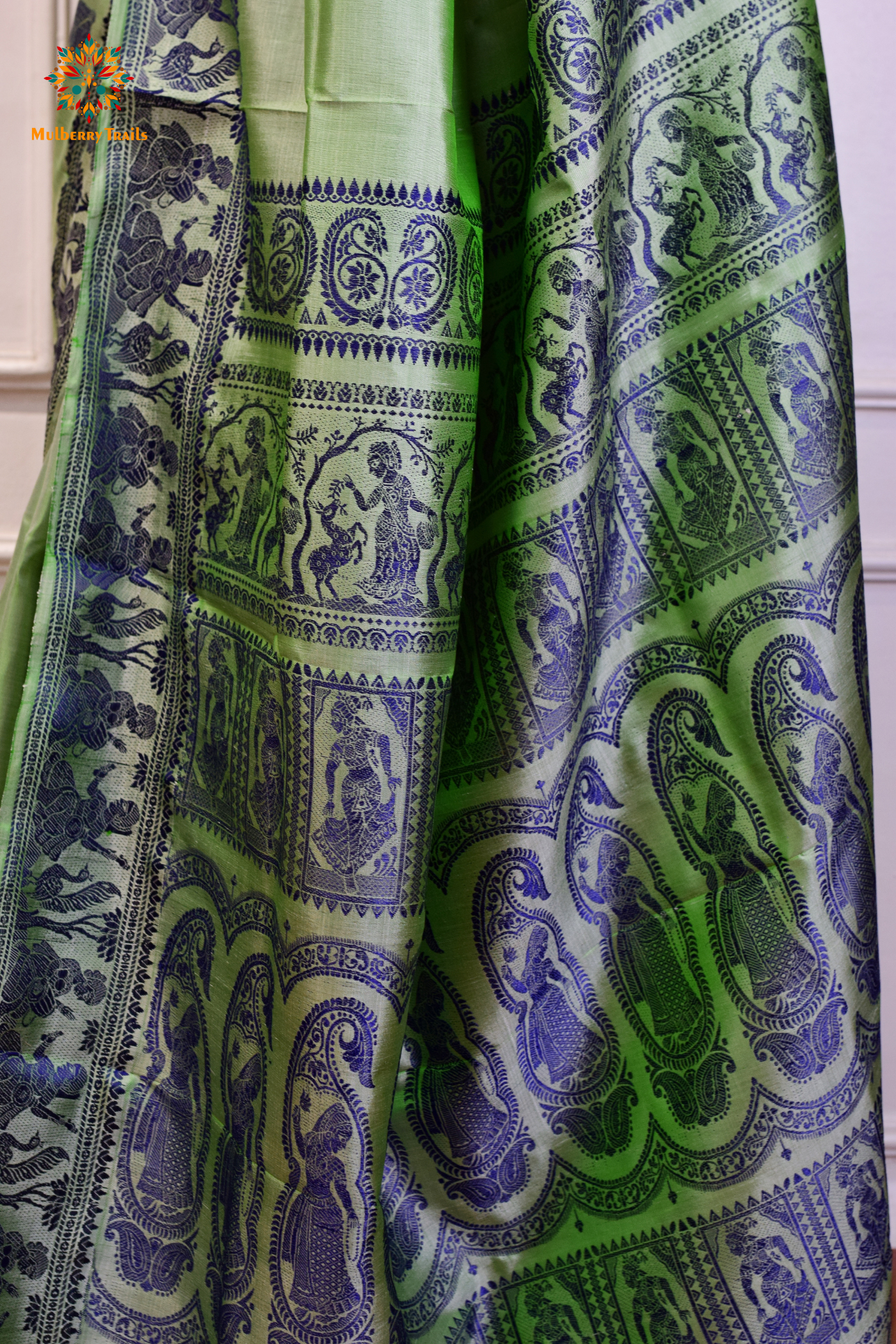 A woman wearing a Sage Green Baluchari Pure SIlk saree. purple baluchari silk , bengal silk saree with deer motif on pallu and ramayan, mahabharat motifs on pallu. This is a soft pure silk saree suitable for weddings, parties, festivities. suitable for Durga Puja shopping enthusiasts and diwali festival. 