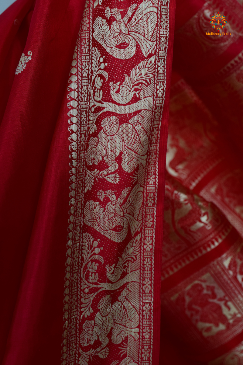 A woman wearing a Red Baluchari Pure SIlk saree. Red baluchari silk , bengal silk saree with deer motif on pallu and ramayan, mahabharat motifs on pallu. This is a soft pure silk saree suitable for weddings, parties, festivities. suitable for Durga Puja shopping enthusiasts and diwali festival. 