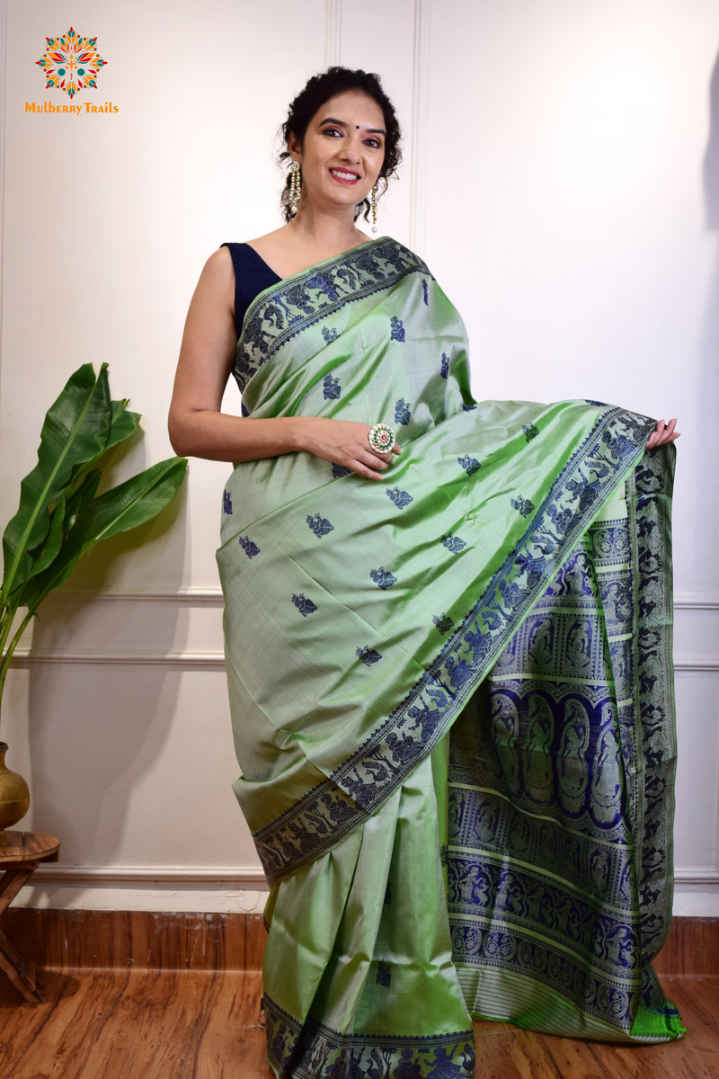 A woman wearing a Sage Green Baluchari Pure SIlk saree. purple baluchari silk , bengal silk saree with deer motif on pallu and ramayan, mahabharat motifs on pallu. This is a soft pure silk saree suitable for weddings, parties, festivities. suitable for Durga Puja shopping enthusiasts and diwali festival. 