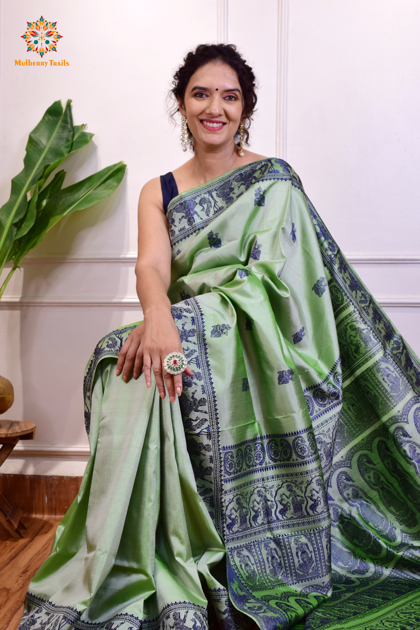 A woman wearing a Sage Green Baluchari Pure SIlk saree. purple baluchari silk , bengal silk saree with deer motif on pallu and ramayan, mahabharat motifs on pallu. This is a soft pure silk saree suitable for weddings, parties, festivities. suitable for Durga Puja shopping enthusiasts and diwali festival. 