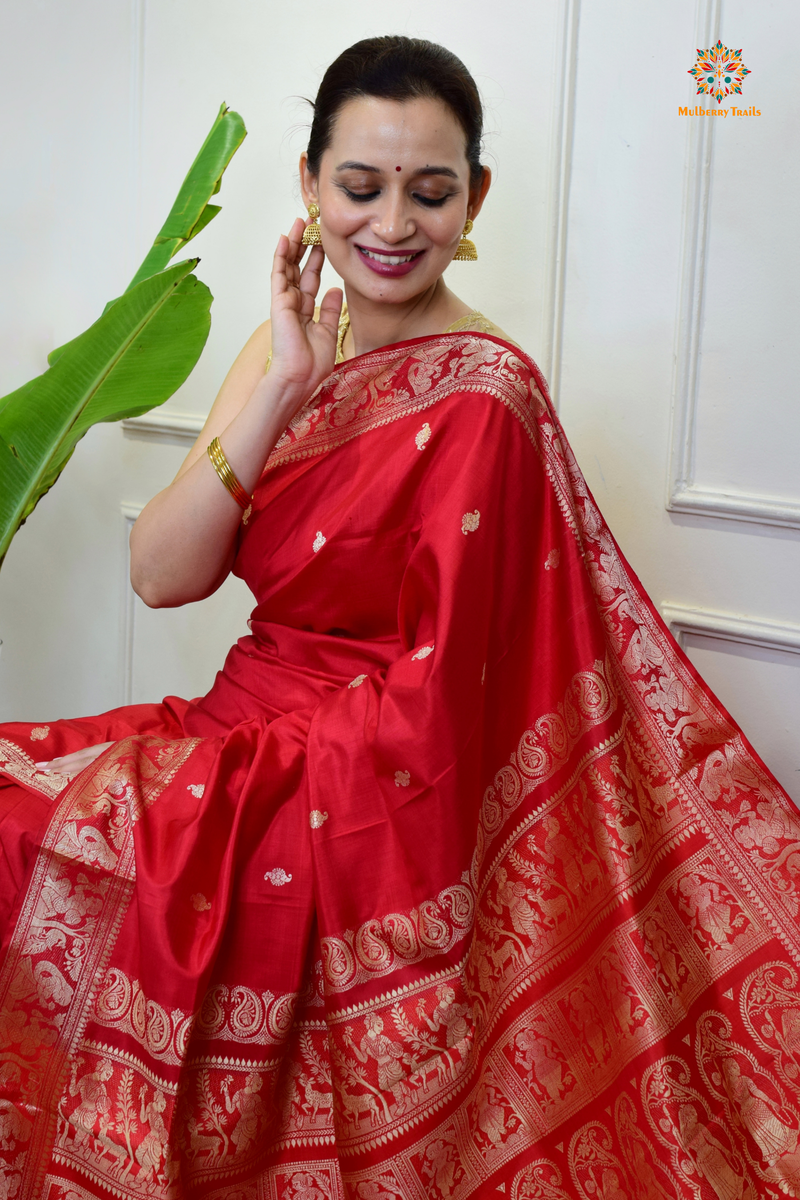 A woman wearing a Red Baluchari Pure SIlk saree. Red baluchari silk , bengal silk saree with deer motif on pallu and ramayan, mahabharat motifs on pallu. This is a soft pure silk saree suitable for weddings, parties, festivities. suitable for Durga Puja shopping enthusiasts and diwali festival. 