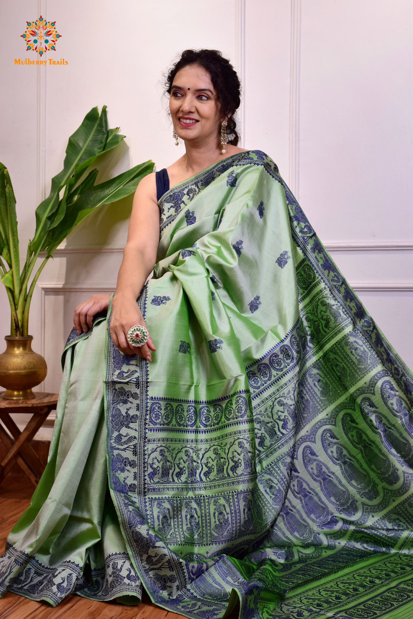 A woman wearing a Sage Green Baluchari Pure SIlk saree. purple baluchari silk , bengal silk saree with deer motif on pallu and ramayan, mahabharat motifs on pallu. This is a soft pure silk saree suitable for weddings, parties, festivities. suitable for Durga Puja shopping enthusiasts and diwali festival. 