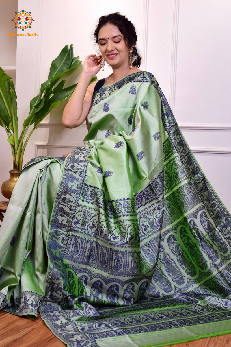 A woman wearing a Sage Green Baluchari Pure SIlk saree. purple baluchari silk , bengal silk saree with deer motif on pallu and ramayan, mahabharat motifs on pallu. This is a soft pure silk saree suitable for weddings, parties, festivities. suitable for Durga Puja shopping enthusiasts and diwali festival. 