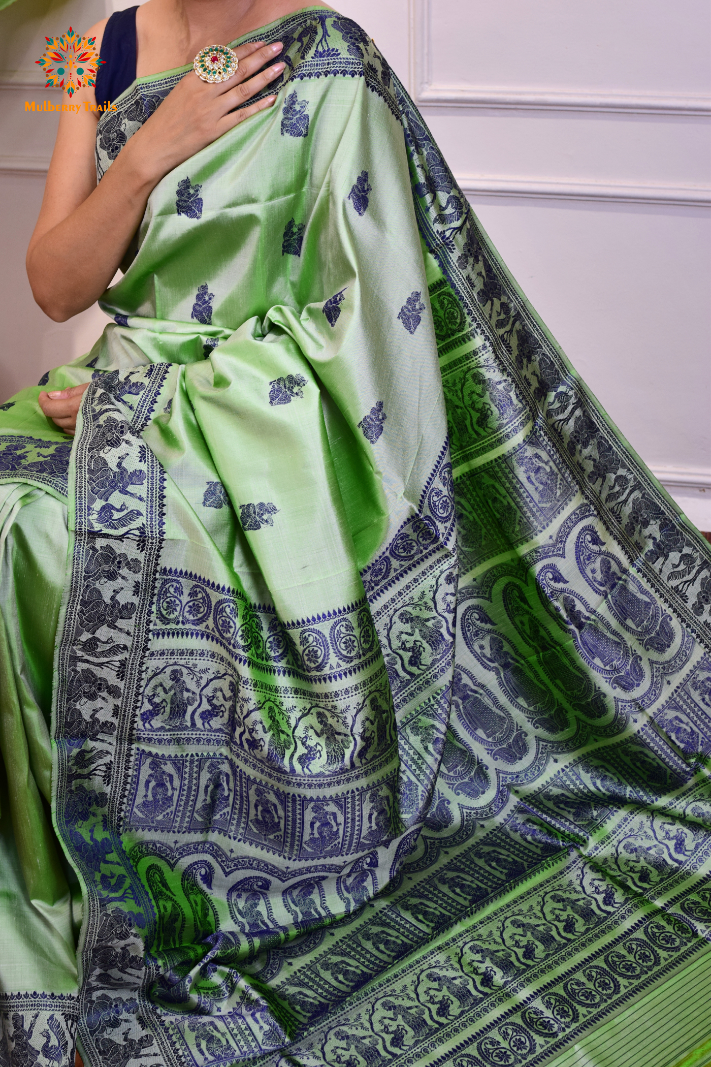 A woman wearing a Sage Green Baluchari Pure SIlk saree. purple baluchari silk , bengal silk saree with deer motif on pallu and ramayan, mahabharat motifs on pallu. This is a soft pure silk saree suitable for weddings, parties, festivities. suitable for Durga Puja shopping enthusiasts and diwali festival. 