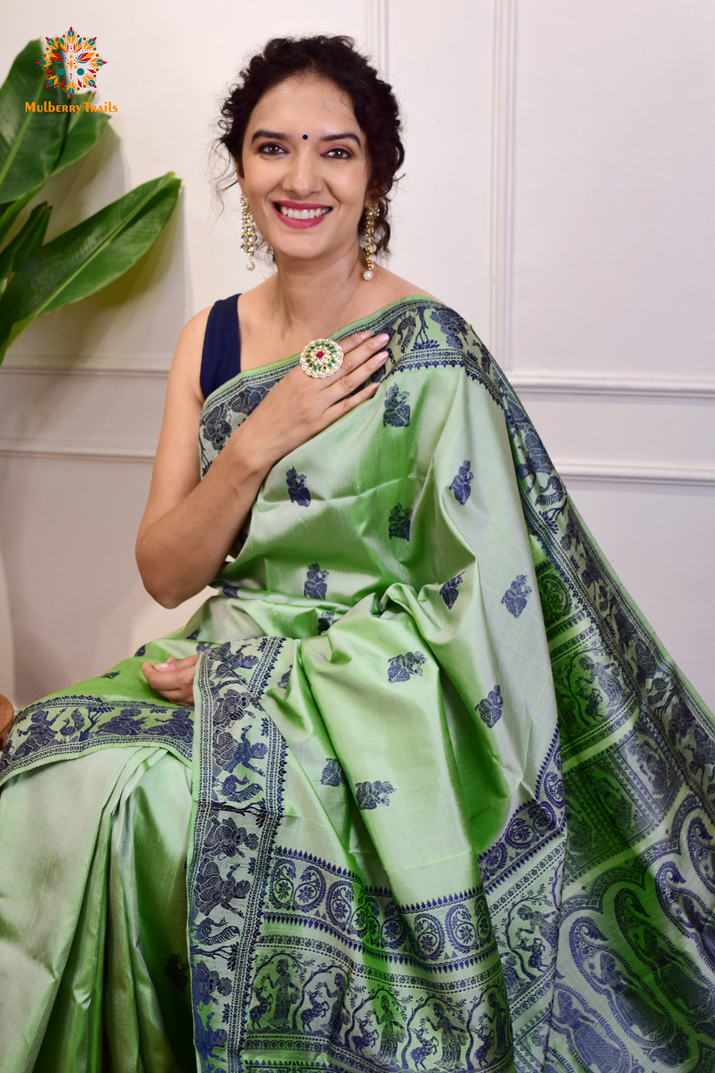 A woman wearing a Sage Green Baluchari Pure SIlk saree. purple baluchari silk , bengal silk saree with deer motif on pallu and ramayan, mahabharat motifs on pallu. This is a soft pure silk saree suitable for weddings, parties, festivities. suitable for Durga Puja shopping enthusiasts and diwali festival. 