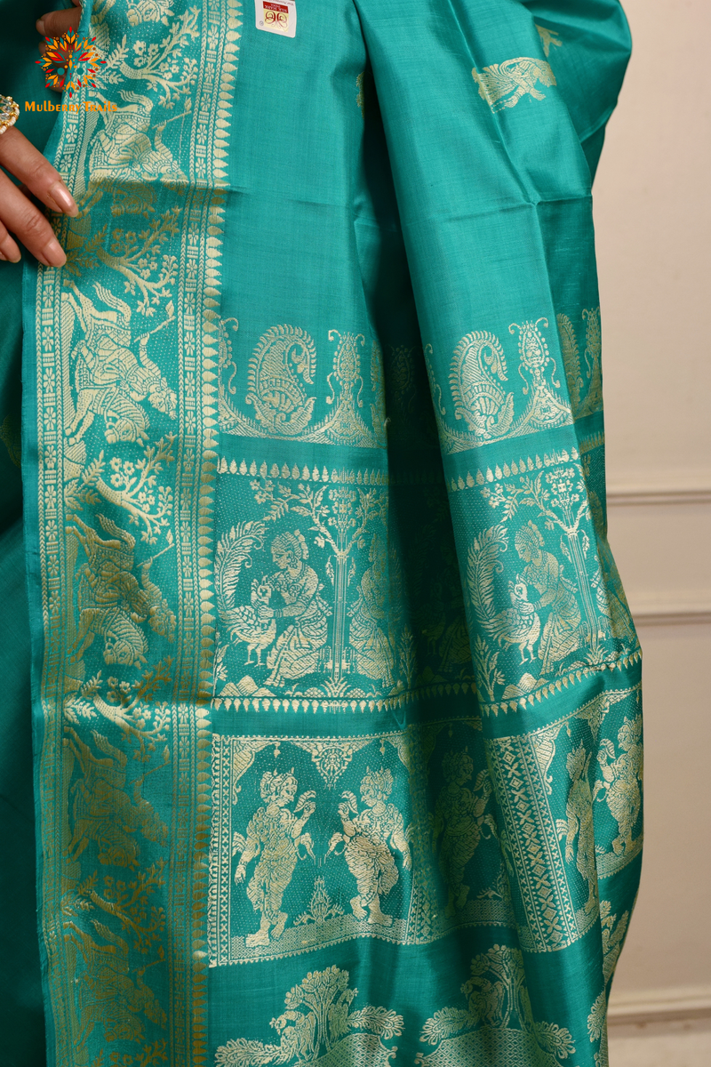 A woman wearing a Aqua Blue Baluchari Pure SIlk saree. purple baluchari silk , bengal silk saree with deer motif on pallu and ramayan, mahabharat motifs on pallu. This is a soft pure silk saree suitable for weddings, parties, festivities. suitable for Durga Puja shopping enthusiasts and diwali festival. 