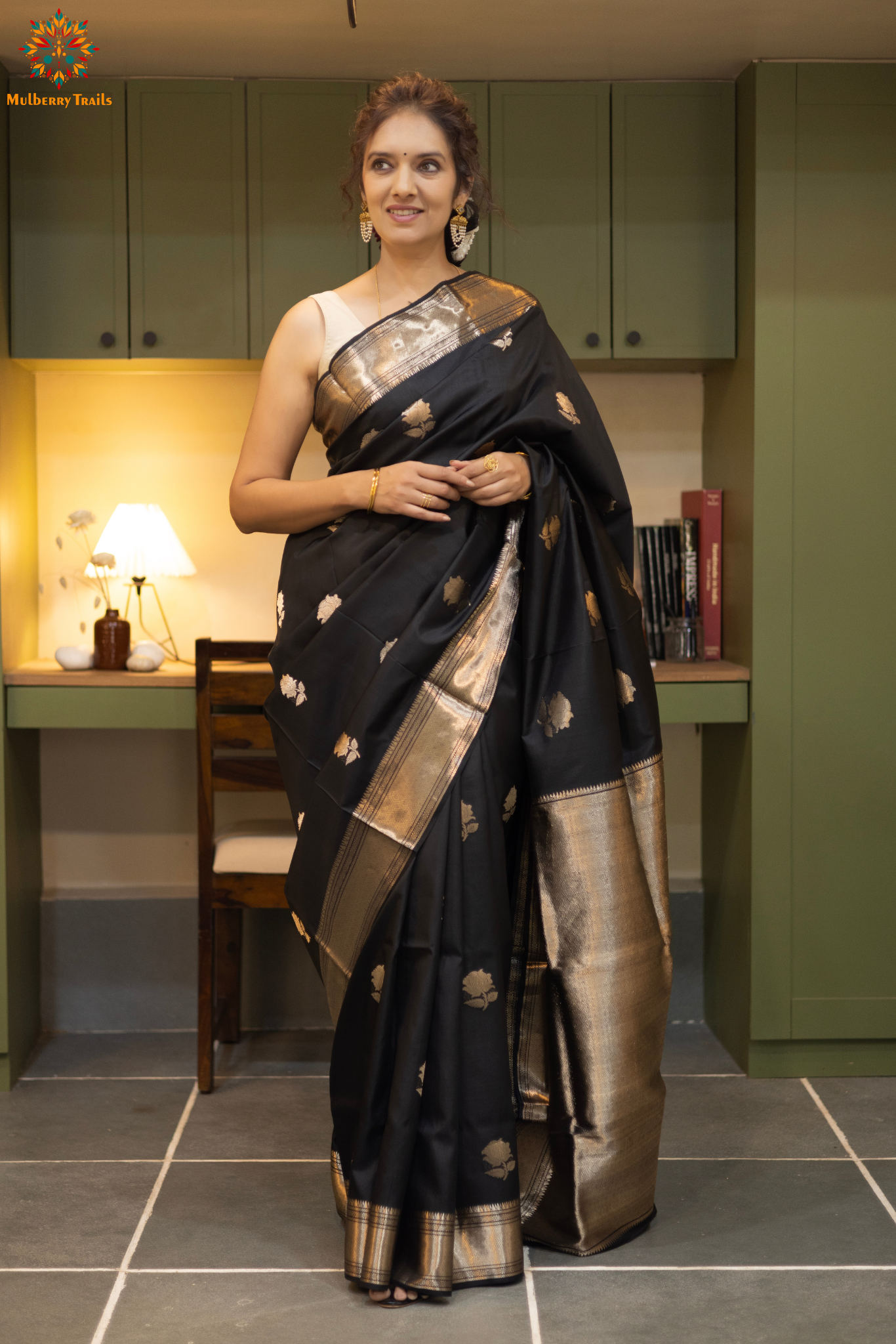 Woman in a black saree with gold patterns sitting indoor. Woman wearing a traditional baluchari saree in a room with a desk and lamp. Woman in a carrot red and silver resham work saree standing indoors with a desk and lamp in the background.

Baluchari – Pure Silk Baluchari Saree

1. “Pure silk Baluchari saree with temple motif weave and Silver resham detailing for a regal look.”

2. “Silk Mark pure silk saree featuring intricate gold resham work motifs and rich texture. 