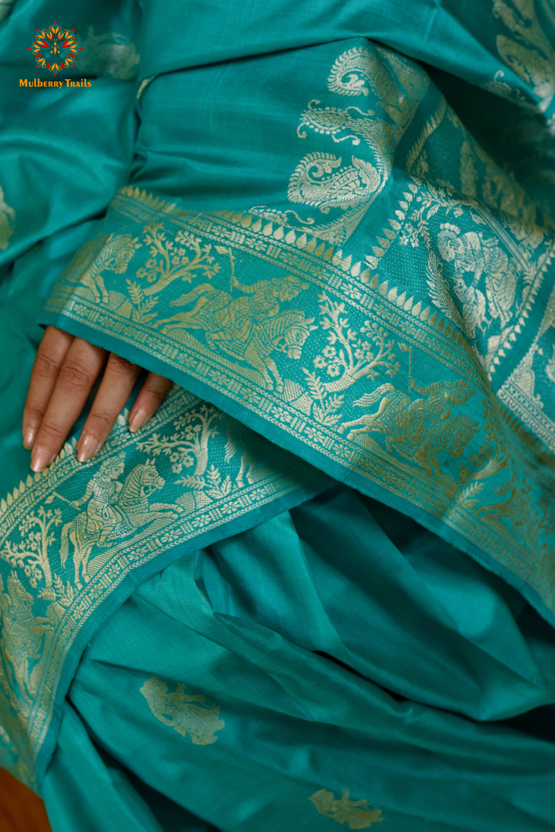 A woman wearing a Aqua Blue Baluchari Pure SIlk saree. purple baluchari silk , bengal silk saree with deer motif on pallu and ramayan, mahabharat motifs on pallu. This is a soft pure silk saree suitable for weddings, parties, festivities. suitable for Durga Puja shopping enthusiasts and diwali festival. 