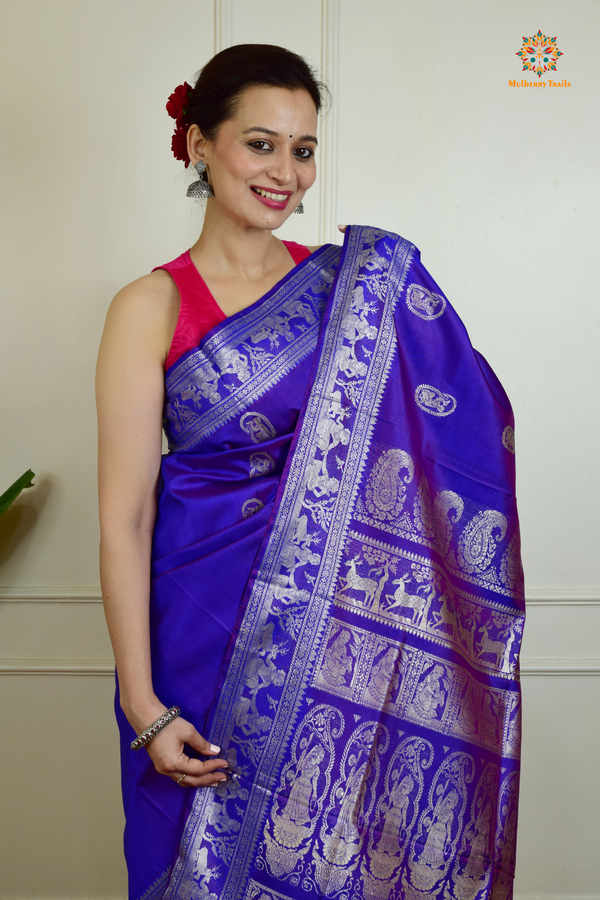 A woman wearing a Purple Baluchari Pure SIlk saree. Purple baluchari silk , bengal silk saree with deer motif on pallu and ramayan, mahabharat motifs on pallu. This is a soft pure silk saree suitable for weddings, parties, festivities. suitable for Durga Puja shopping enthusiasts and diwali festival. 